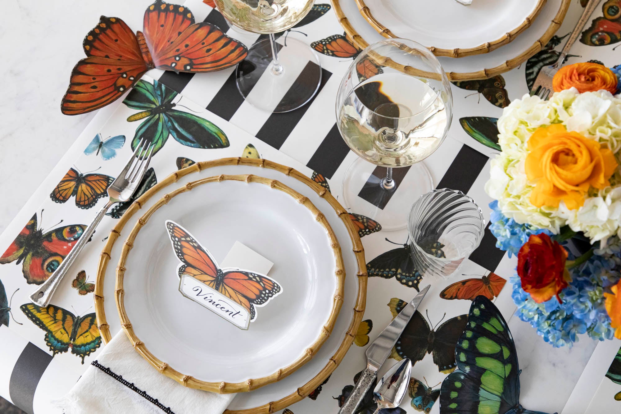 Elegant table setting with butterfly-themed decor and place cards on a black and white striped tablecloth.