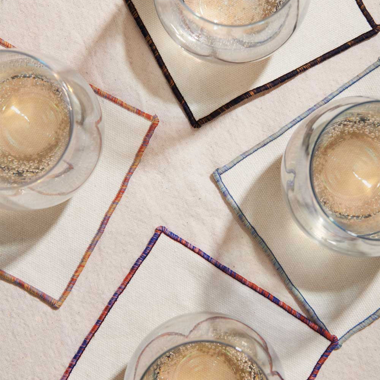 Rainbow Sky Cocktail Napkin Set of 4 displayed with glasses on top, against a beige backbround.