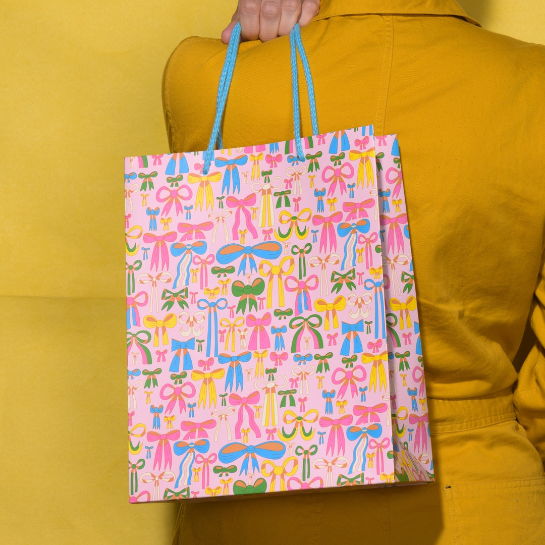 Person holding a pink gift bag with colorful bow pattern against a yellow background