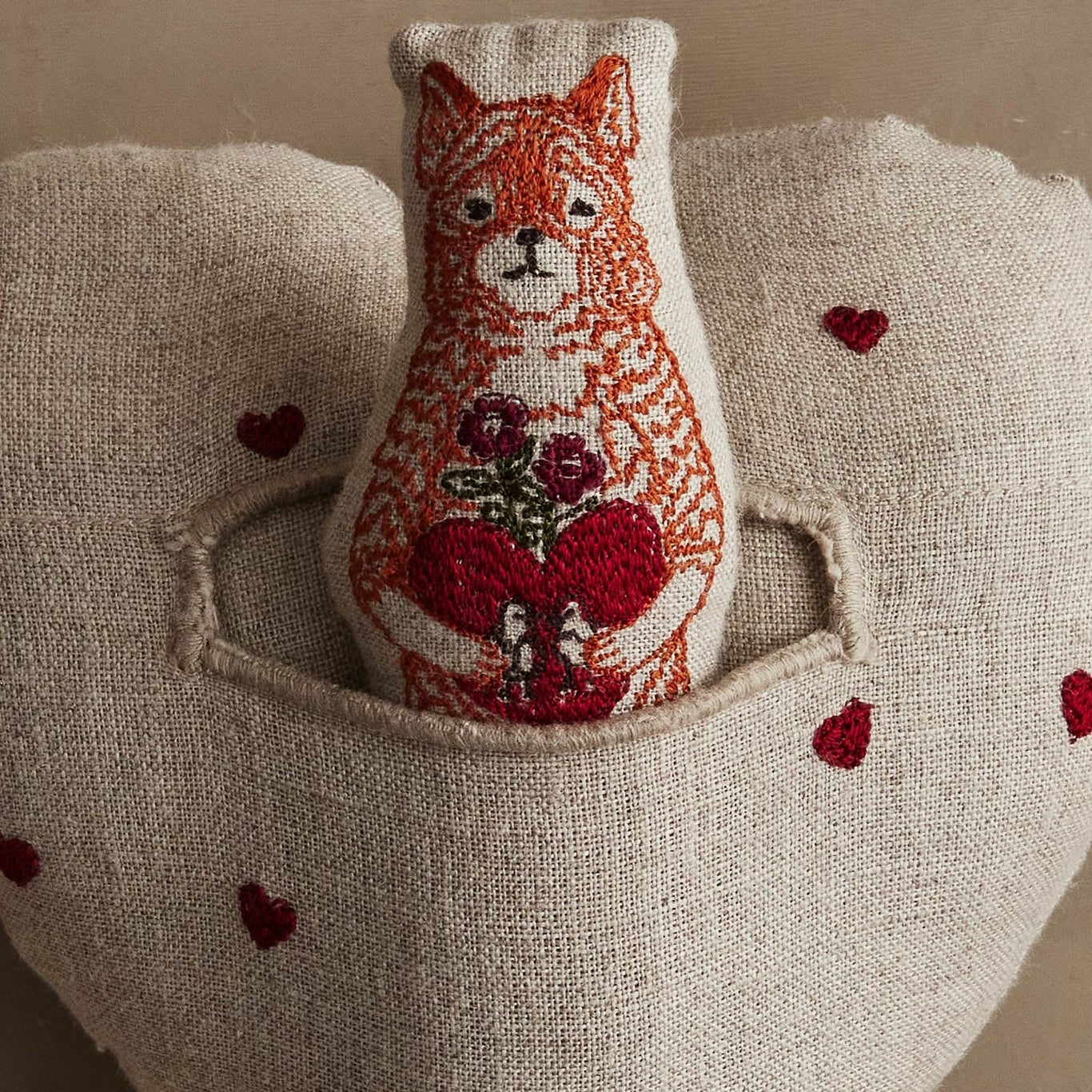 Textile art piece with a fox holding flowers and hearts on a beige background.
