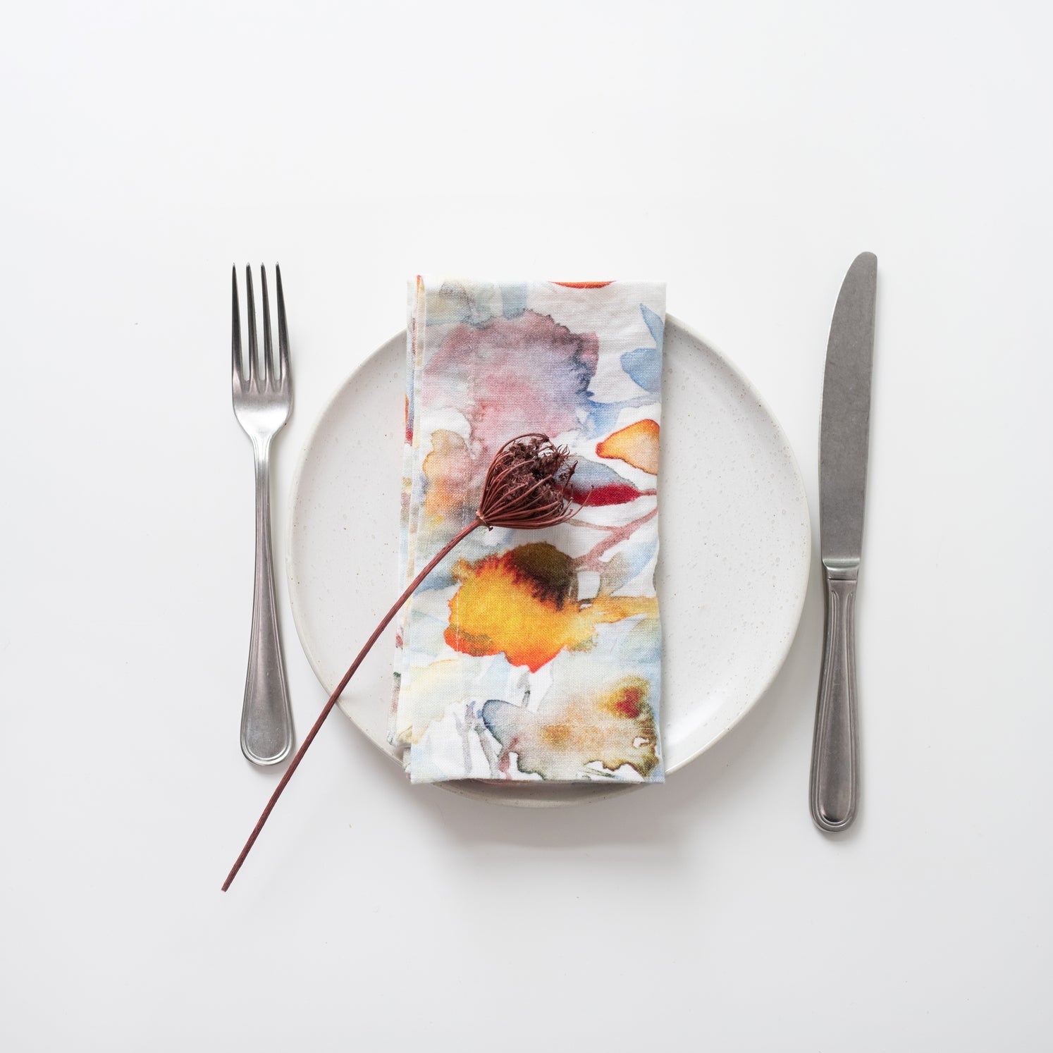 Napkin with floral design on a white plate with cutlery.