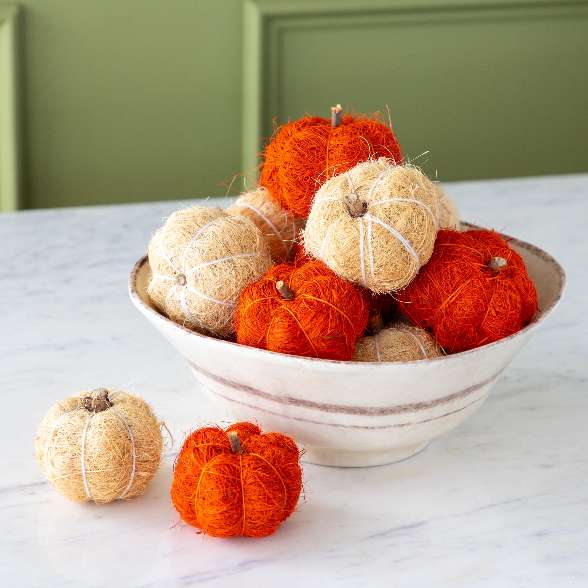 Coco fiber decorative pumpkins in burnt orange and cream in a bowl on a marble table.