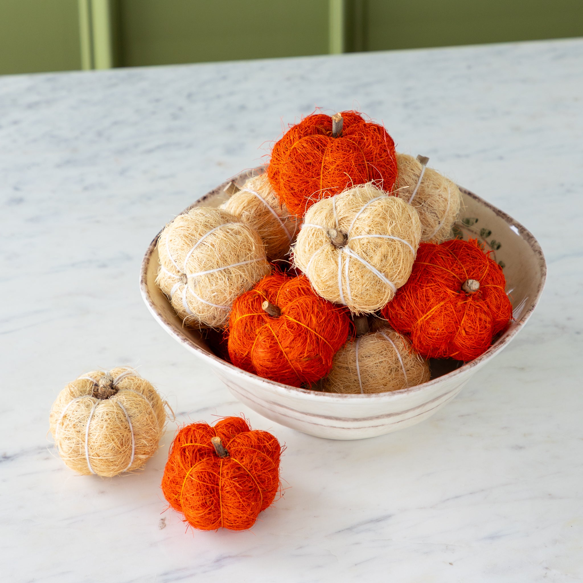 Coco fiber decorative pumpkins in burnt orange and cream in a bowl on a marble table.