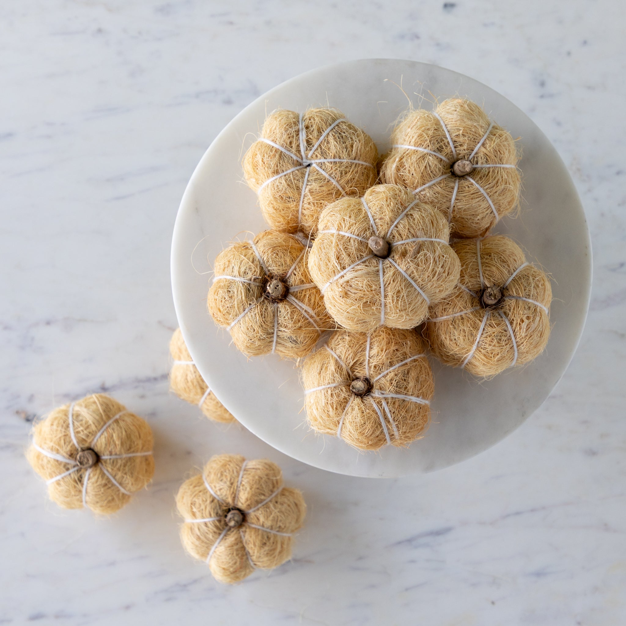 Cream coco fiber pumpkins on a white cake stand with a wooden base against a green wall.