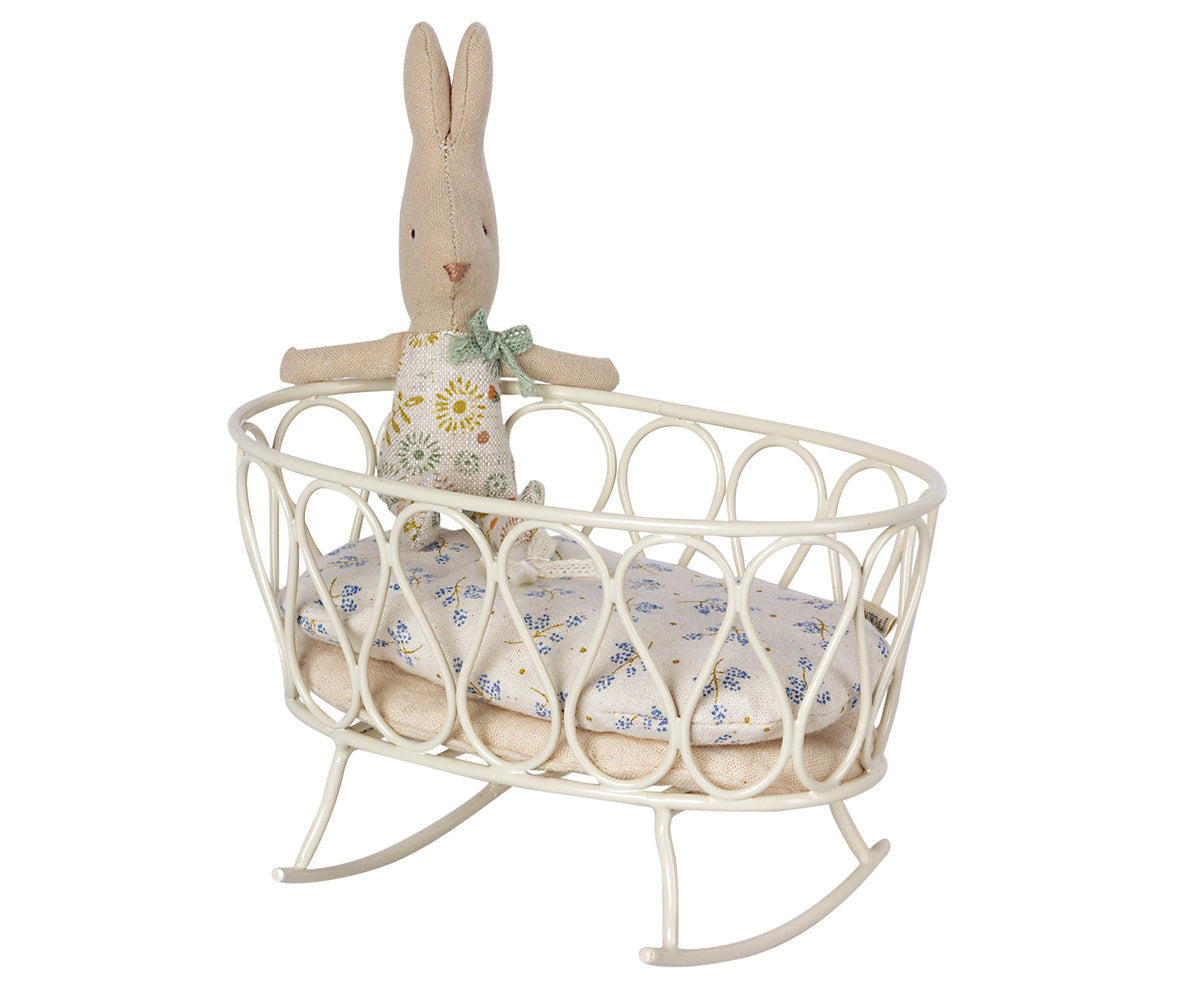 A Maileg stuffed rabbit toy resting on a white Maileg metal cradle against a wall with simple decor.