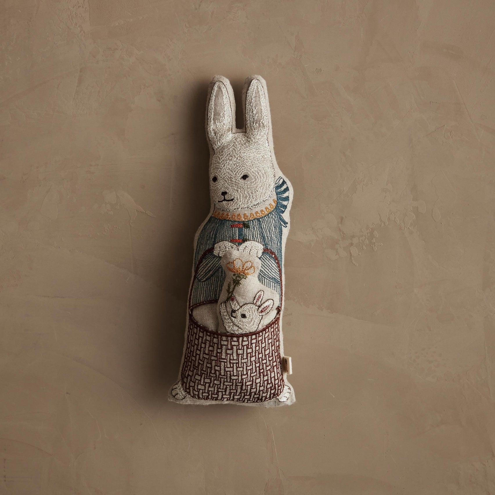 Decorative rabbit plush toy with embroidered design on a beige background.