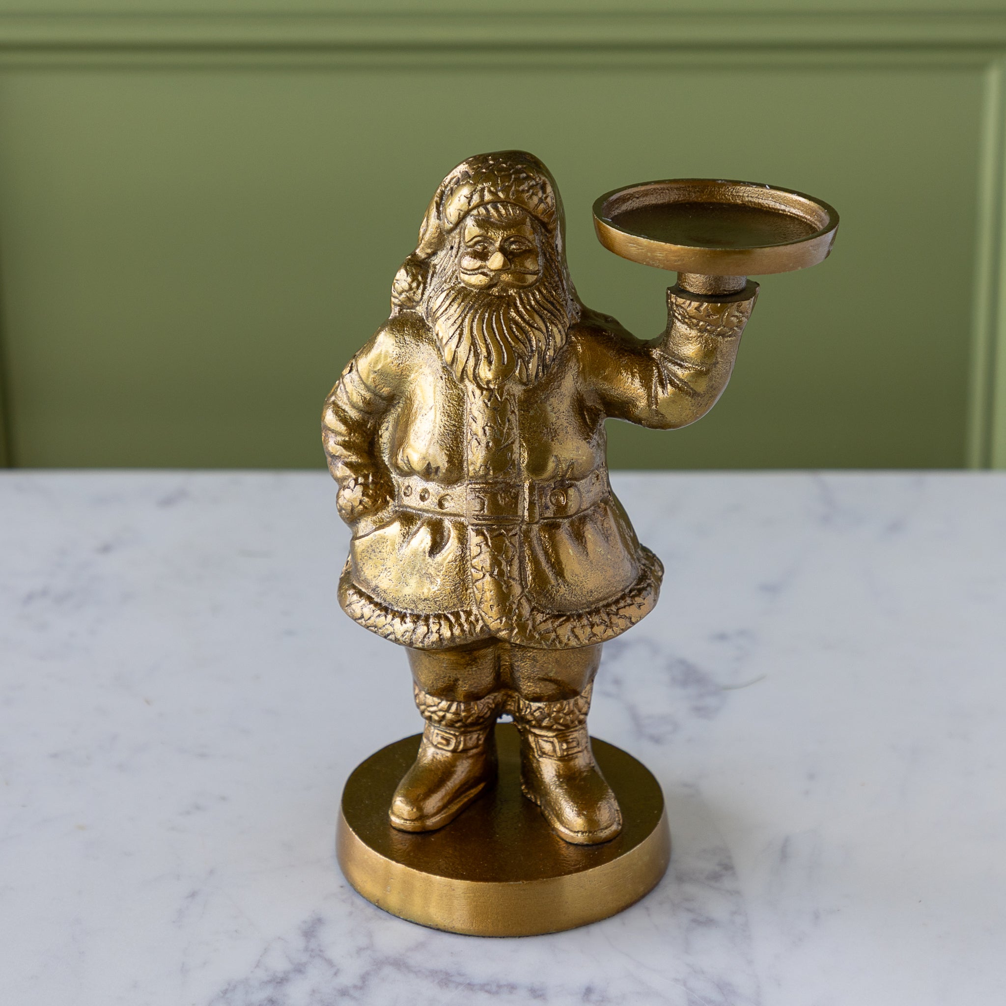 Gold Saint Nick Figurine holding a candle holder on a marble surface with a green wall background.