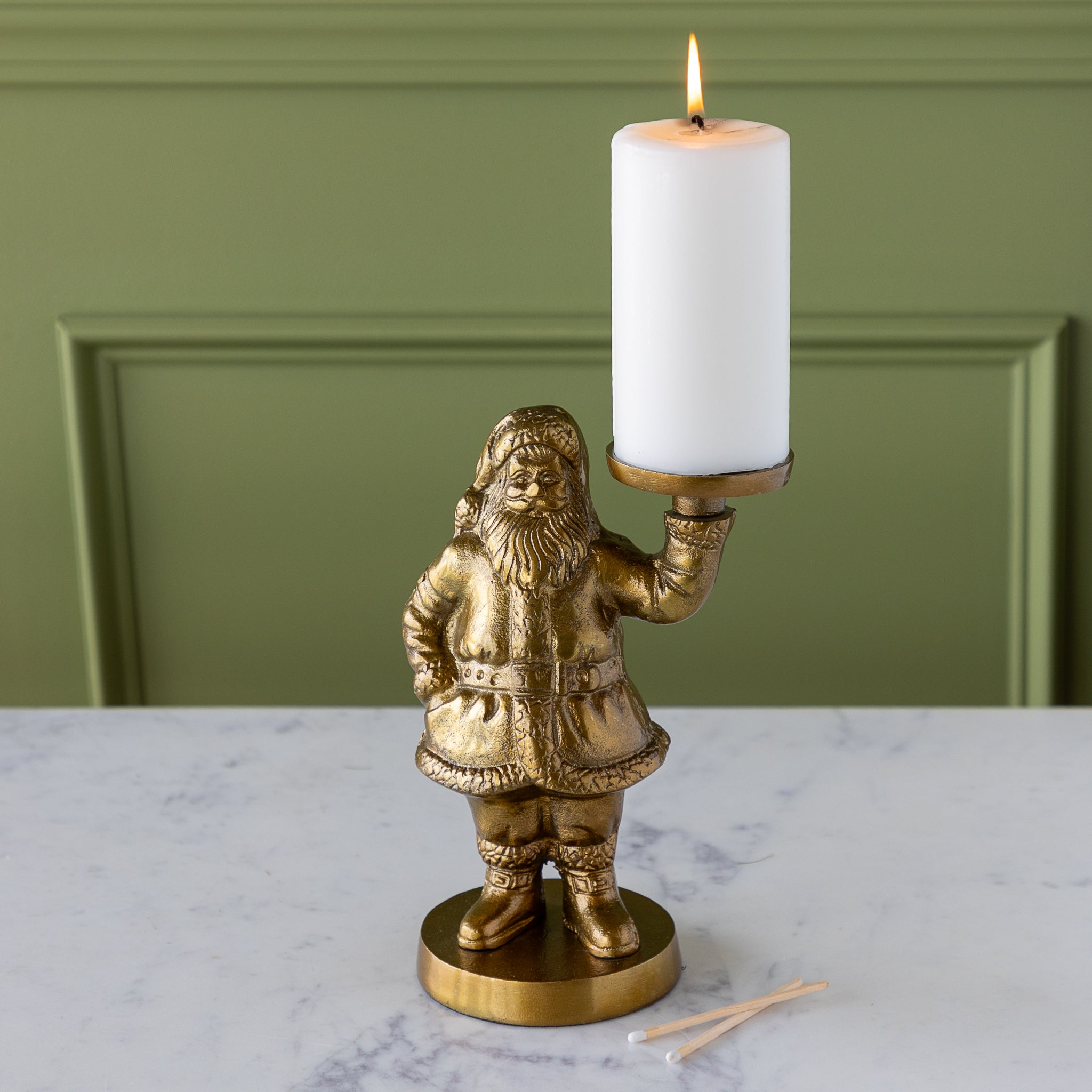 Gold Saint Nick Figurine holding a pillar candle on a marble surface with a green wall background.
