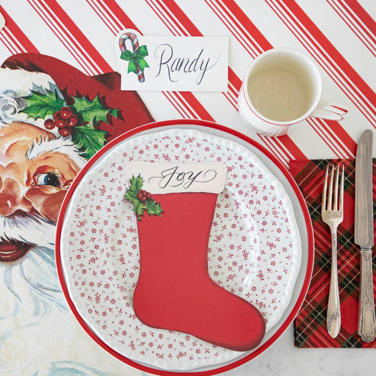 The Stocking Table Accent with "Joy" written on it, resting on a plate, on a Christmas themed table setting.
