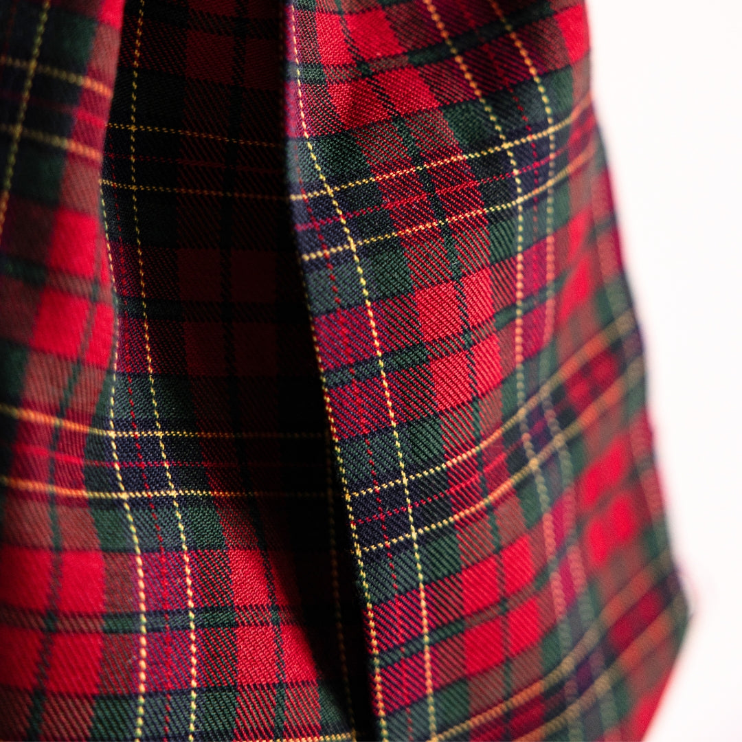 A close-up of a red tartan plaid fabric with dark green and black stripes and thin yellow lines, shown against a white background.