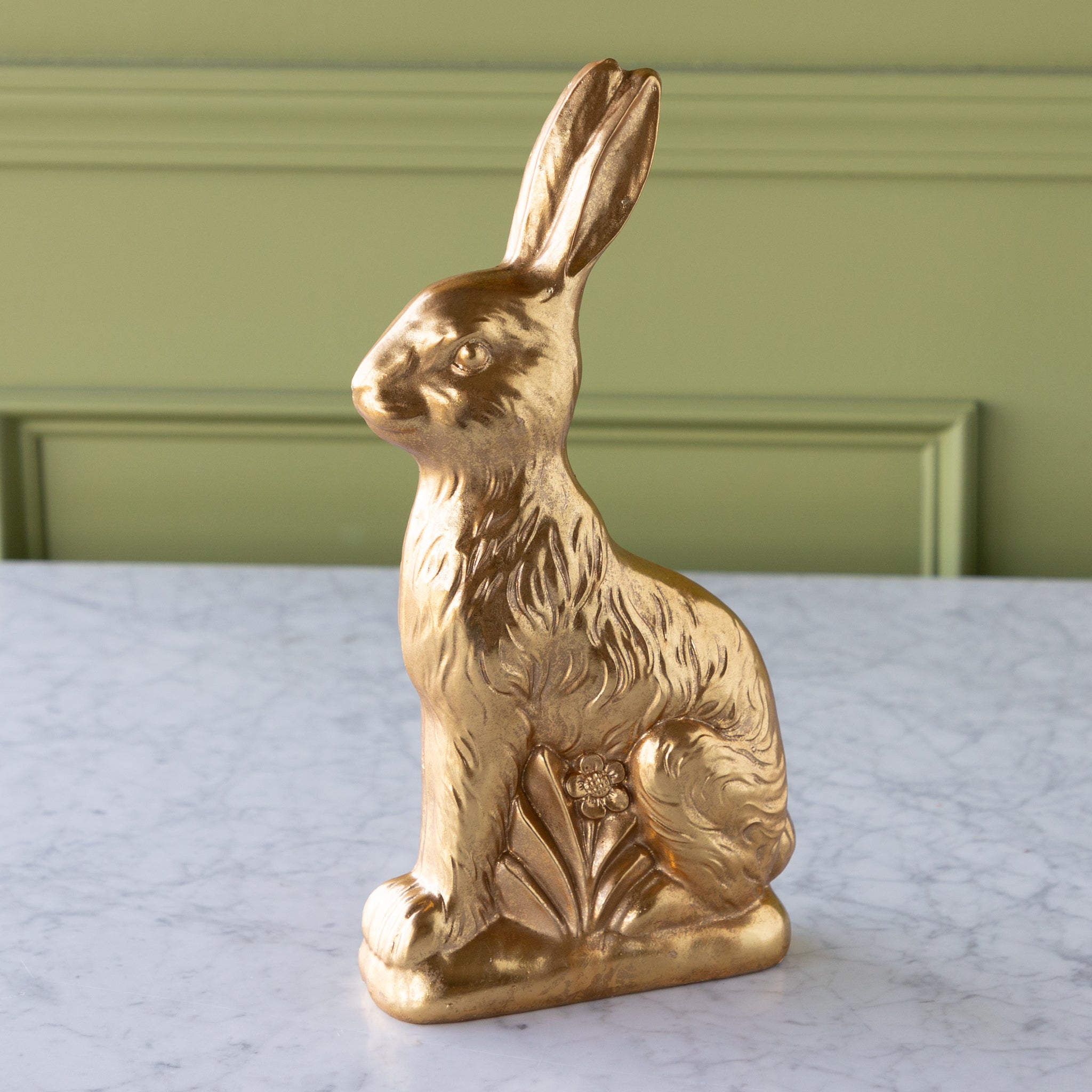 Gold rabbit figurine on a marble surface with a green wall background.