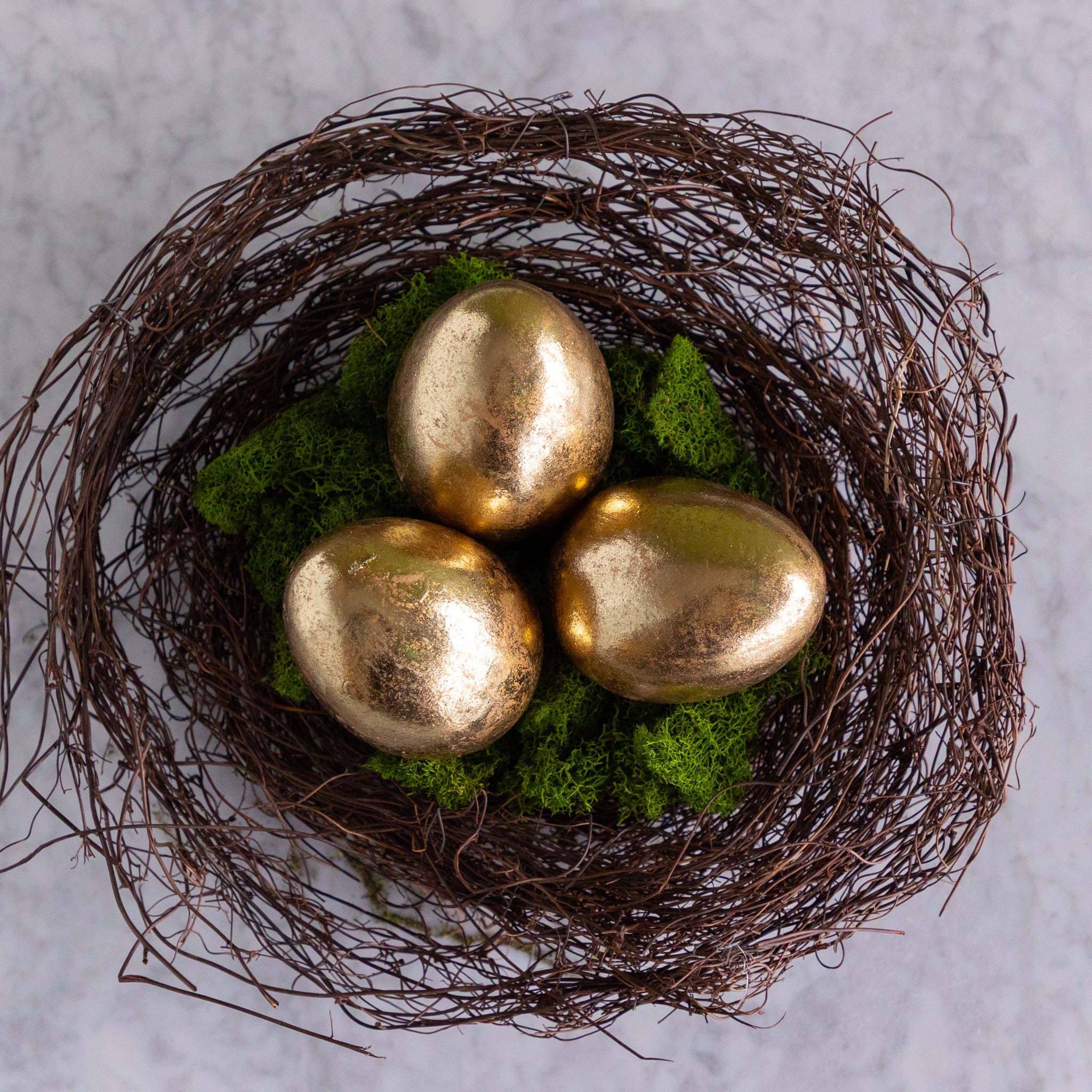 Three gold eggs in a nest on a textured surface.
