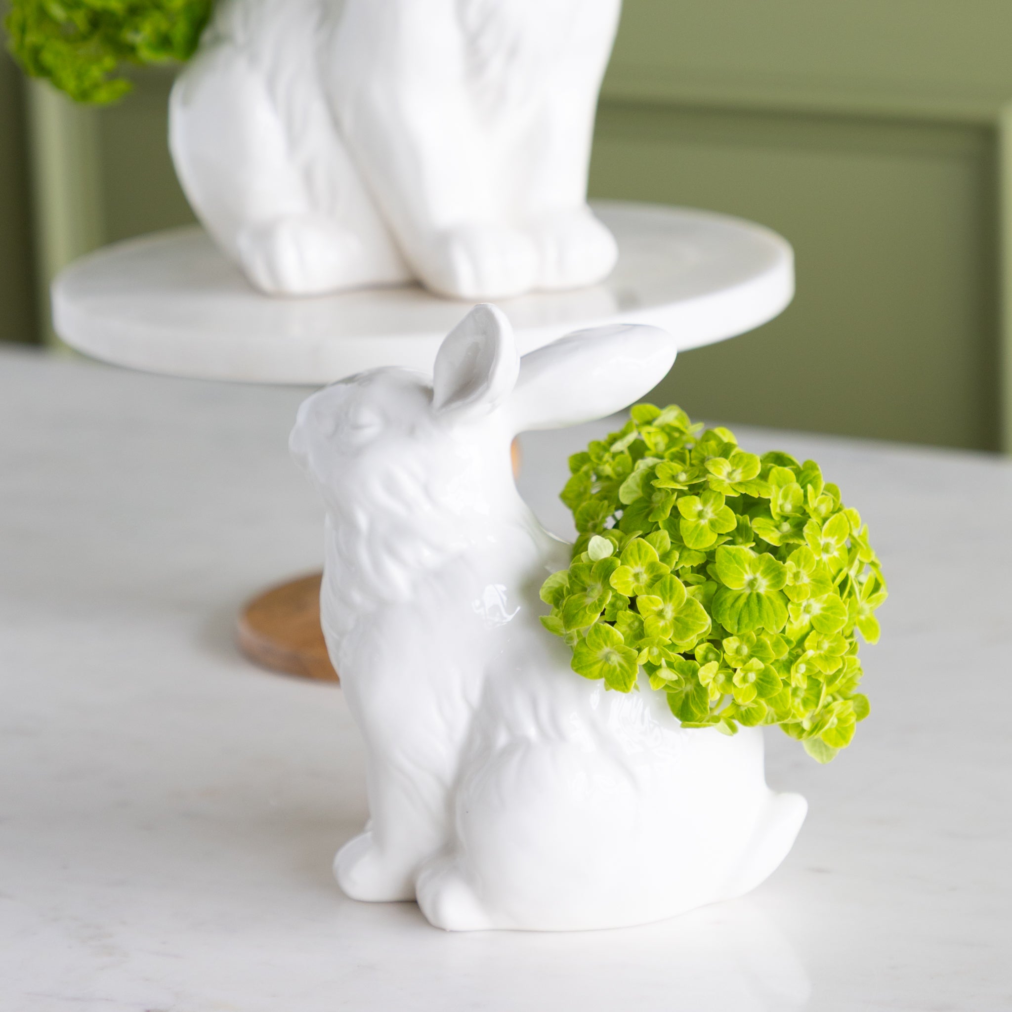 White ceramic rabbit figurine with green flowers on a white surface.
