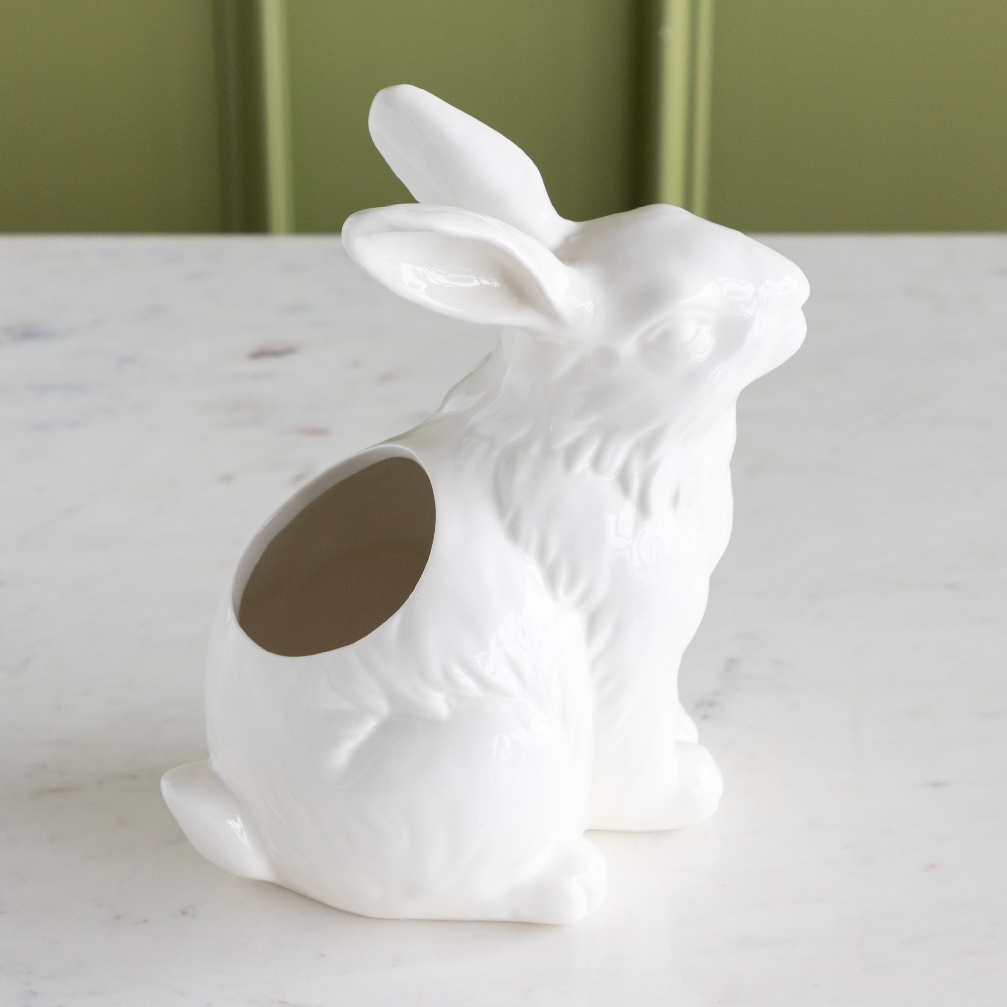 White ceramic rabbit-shaped vase on a marble surface with a green background.