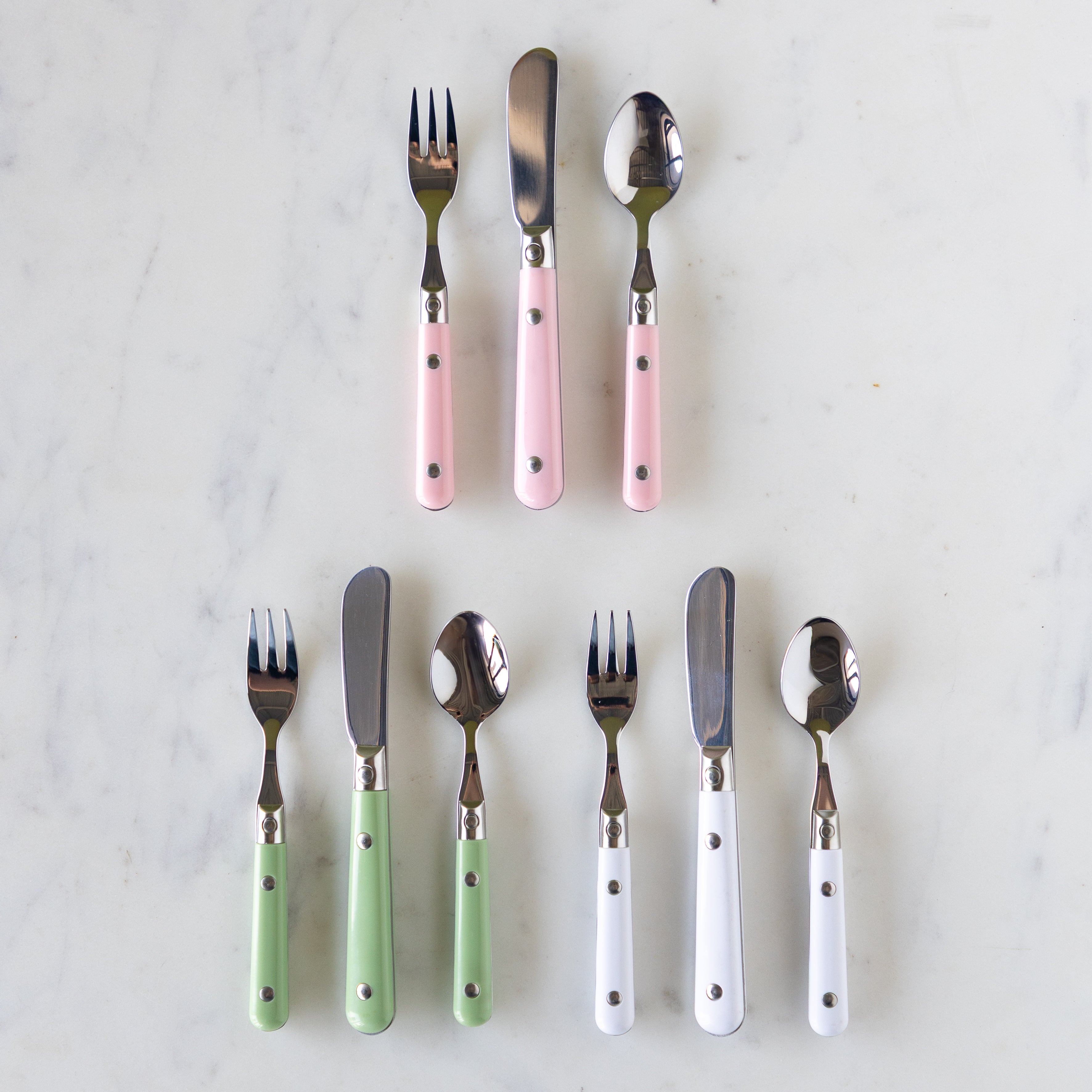 A set of flatware with pink, white, and green handles, including forks, knives, and spoons, displayed on a marble surface.