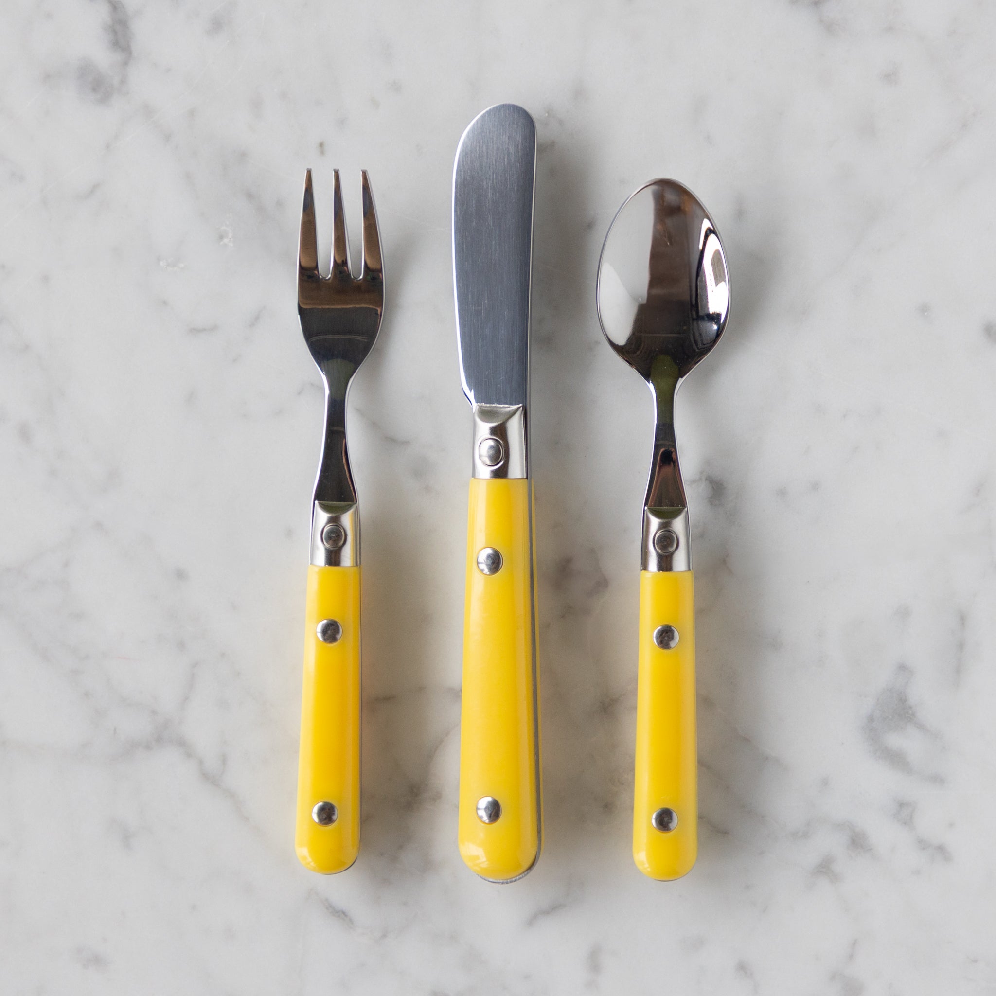 Set of three utensils with yellow handles on a marble surface.
