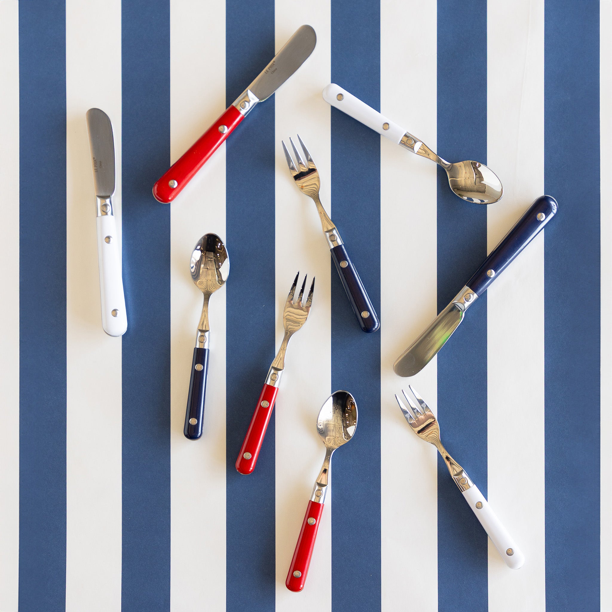 A group pf red, white and blue cutlery scattered on a blue and white striped background.