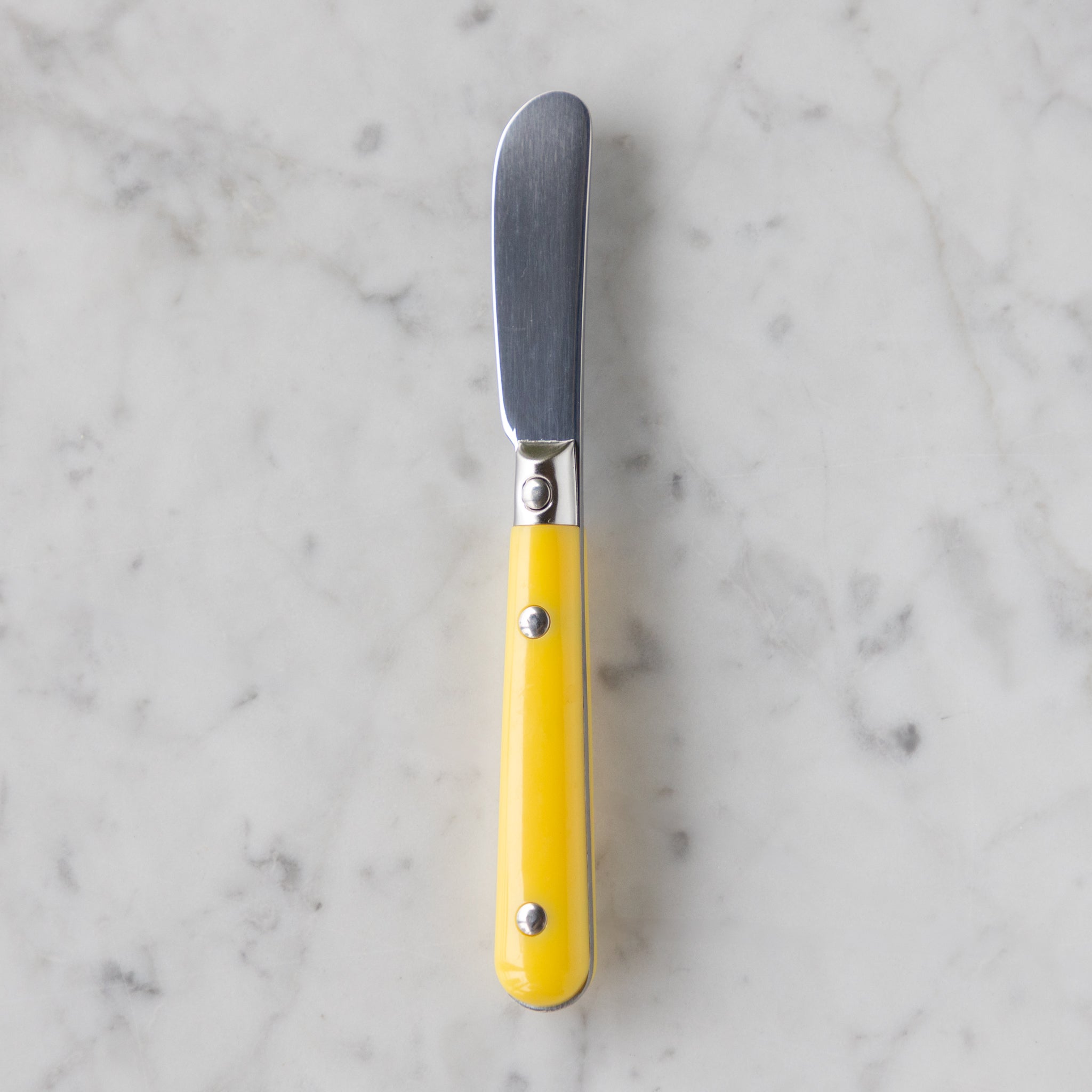 Butter knife with a yellow handle on a marble surface.