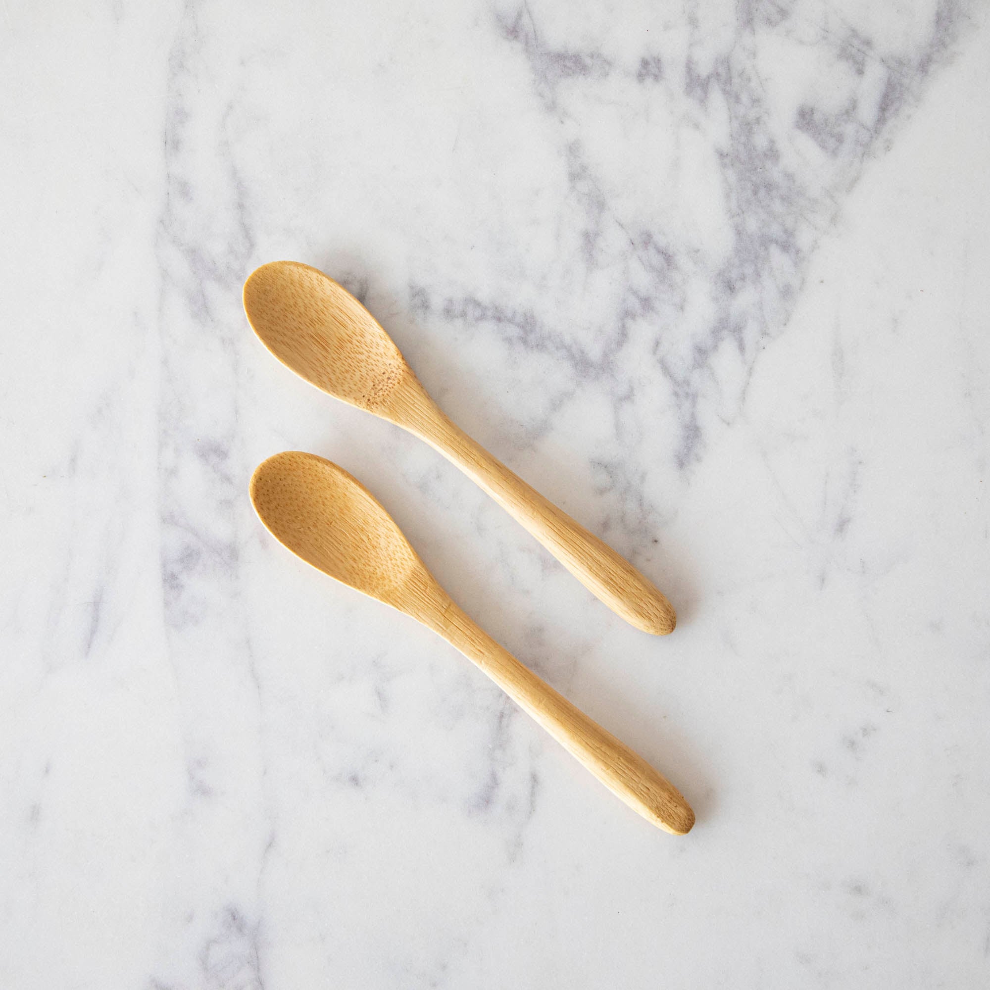 Two Mini Bamboo Spoons on a marble table.
