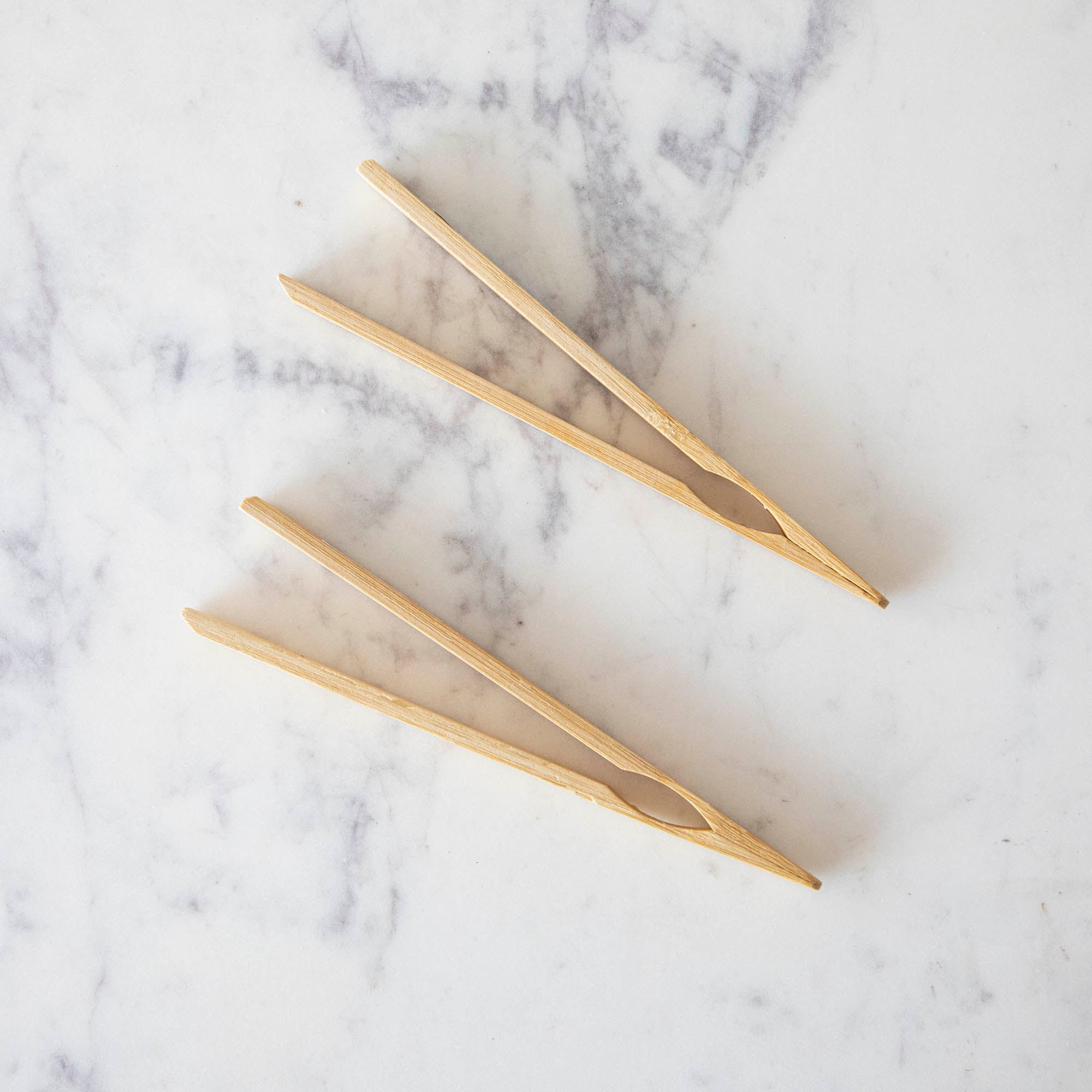 Two mini bamboo tongs on a marble table.