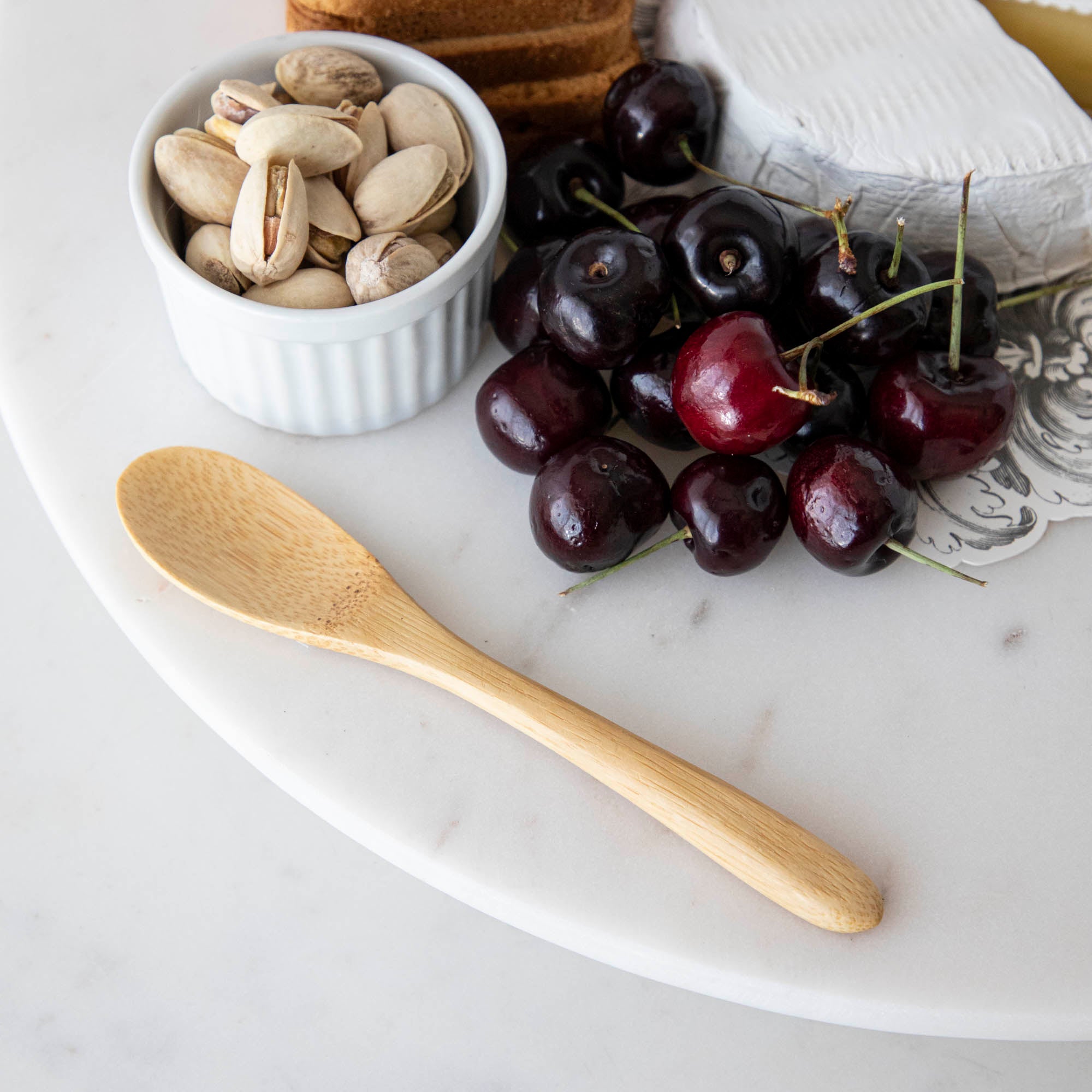 A plate with cheese, fruit, and nuts on it, served with BIA Mini Bamboo Utensils.