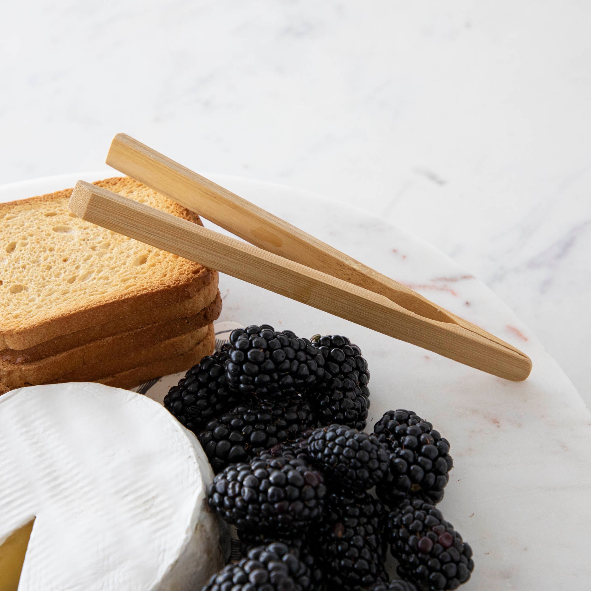 A plate with cheese, fruit, and nuts on it, served with BIA Mini Bamboo Utensils.