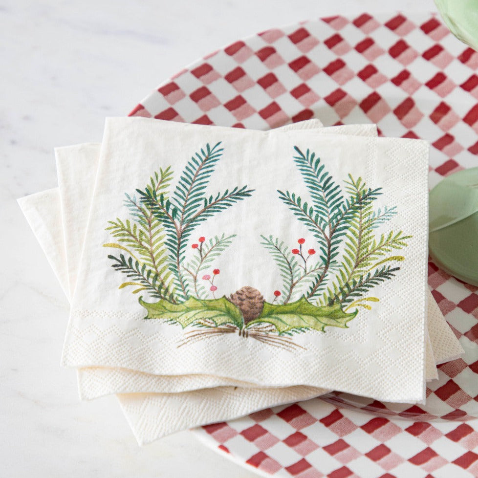 Three Christmas Sprigs Cocktail Napkins fanned out on a red and white plate on a table.