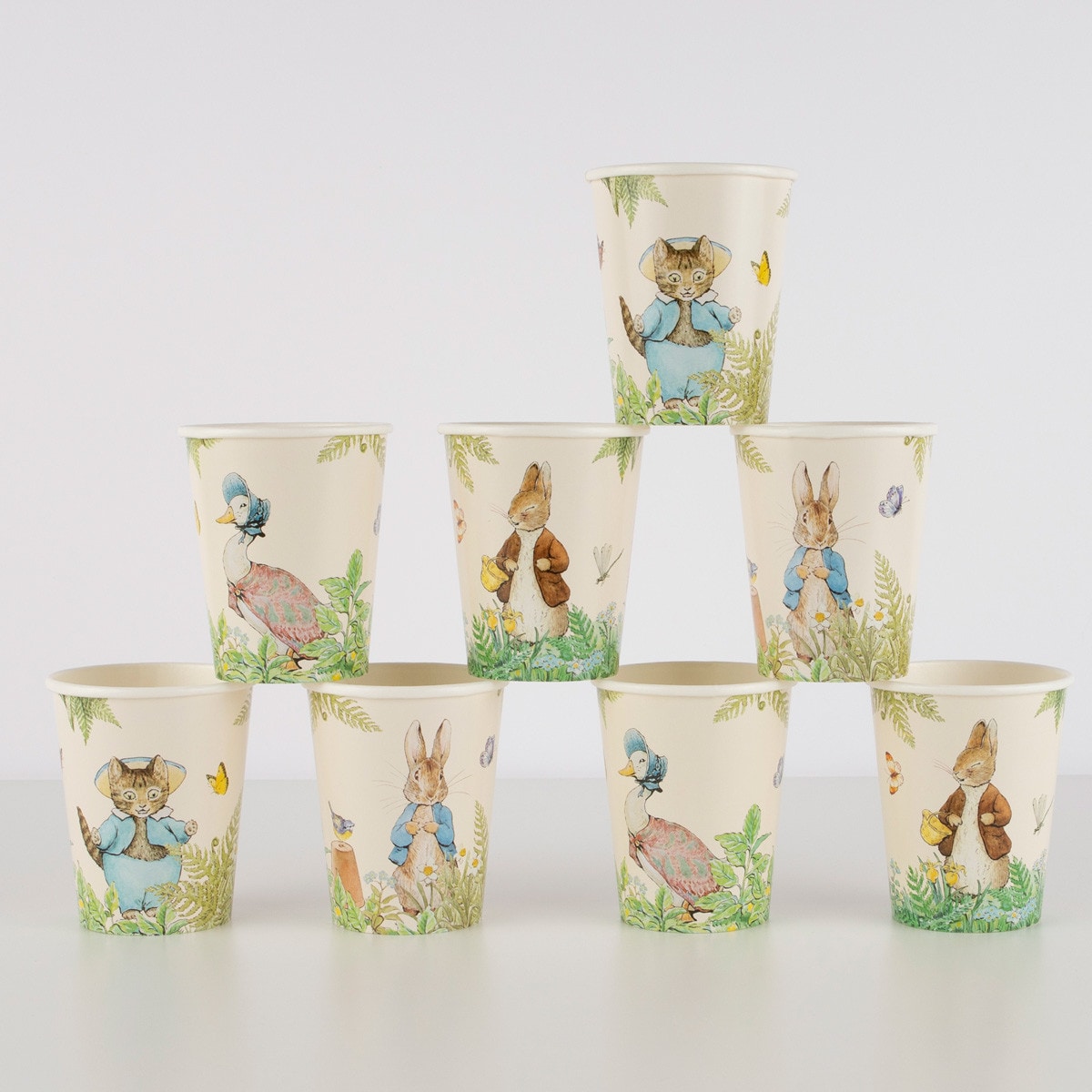 A collection of eight paper cups with illustrations of Peter Rabbit and other characters in a garden setting.