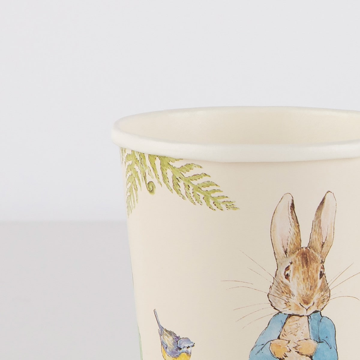 An up-close image of a beige or cream-colored Peter Rabbit illustrated paper cup.