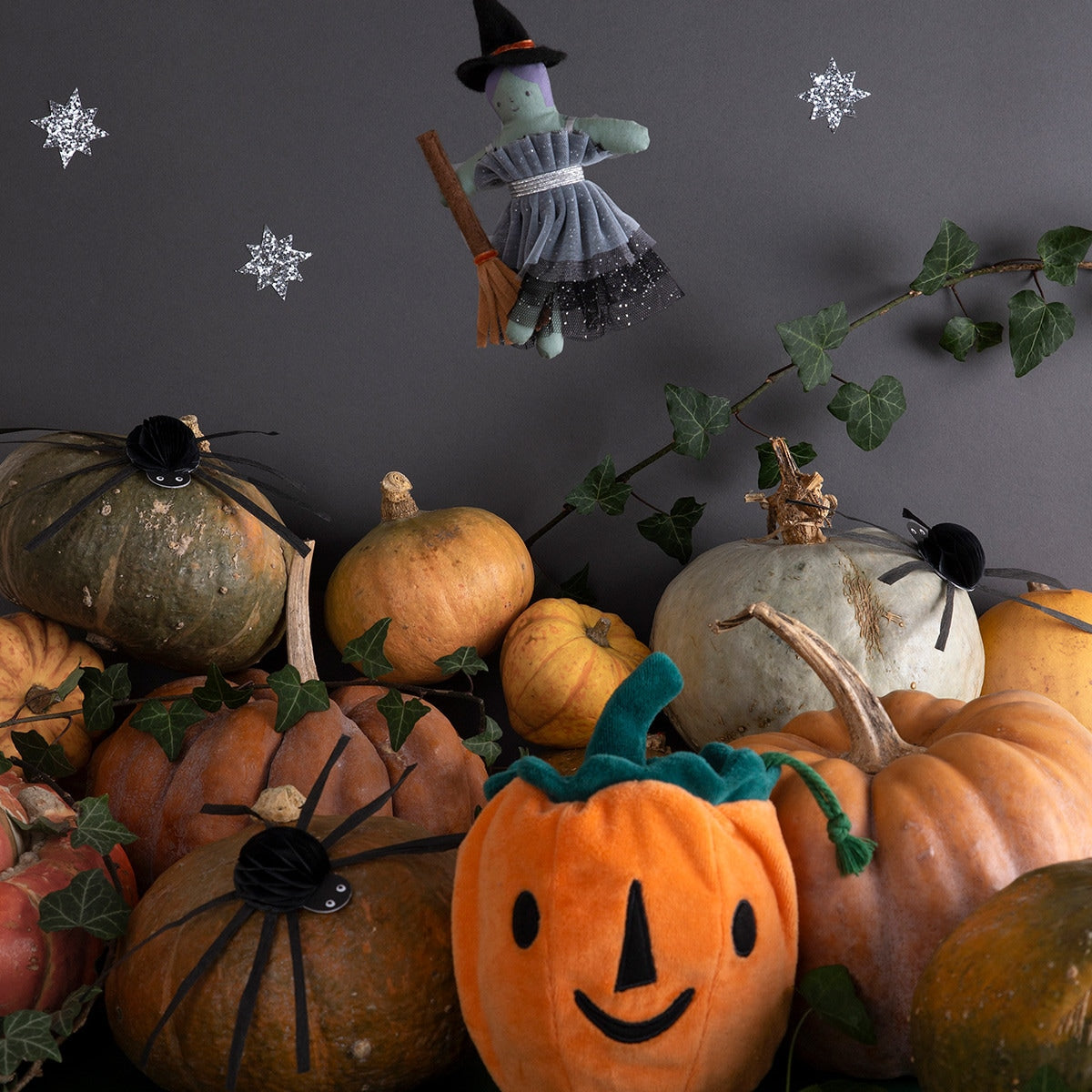 Halloween-themed arrangement with pumpkins, a witch, and ivy on a dark background.