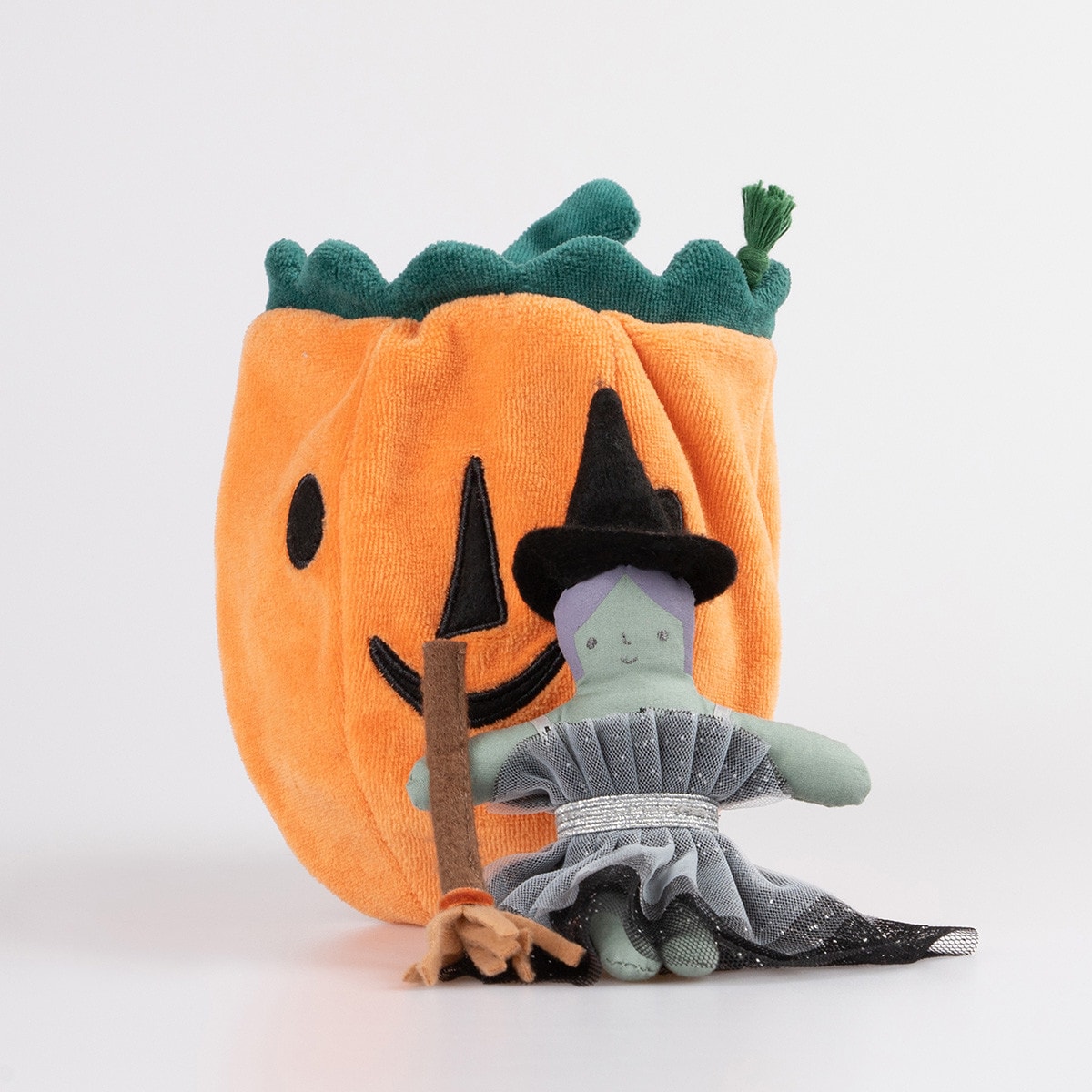 Plush toy witch in front of a pumpkin with a white background