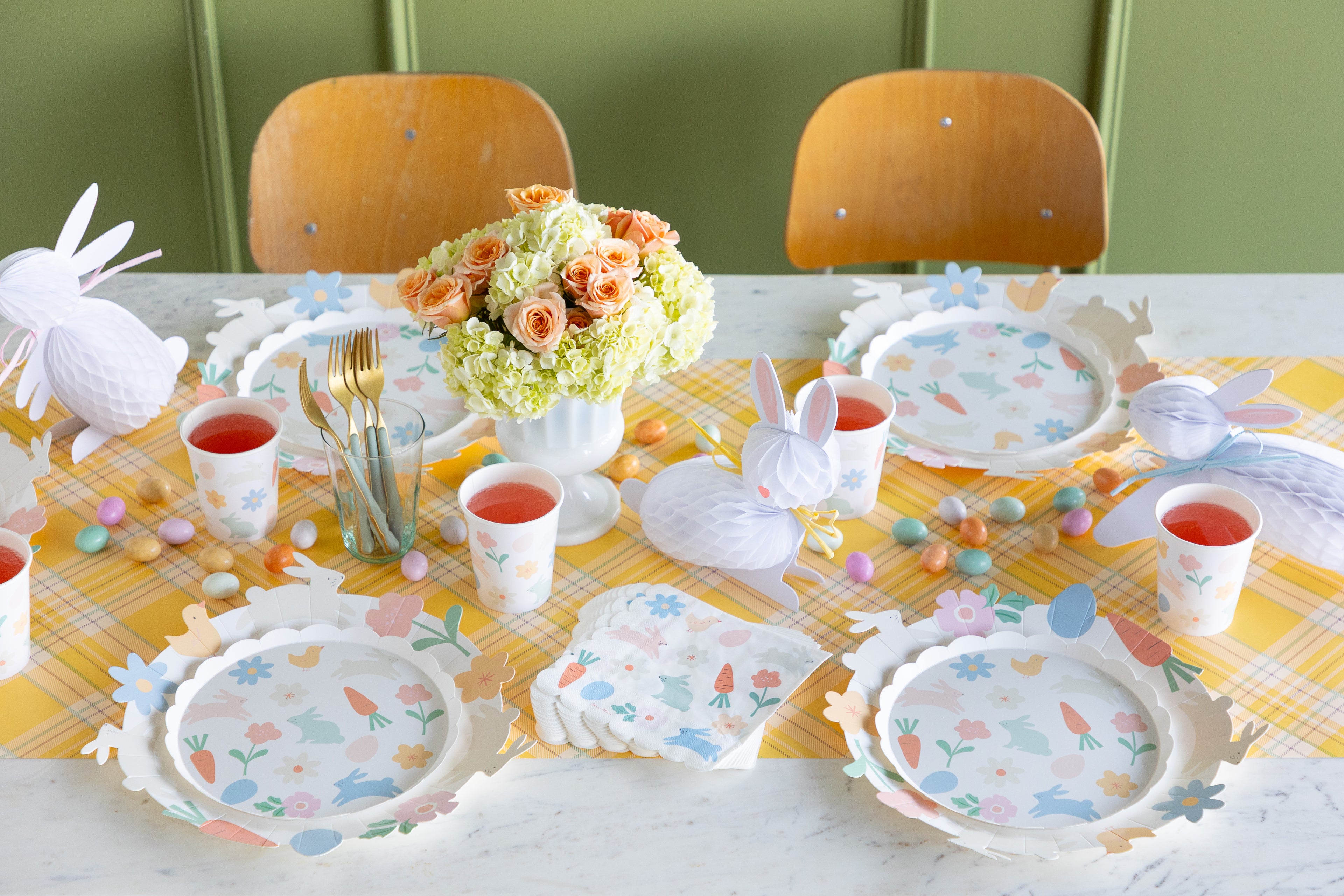 Easter-themed table setting with plates, cups, and decorations on a yellow tablecloth.