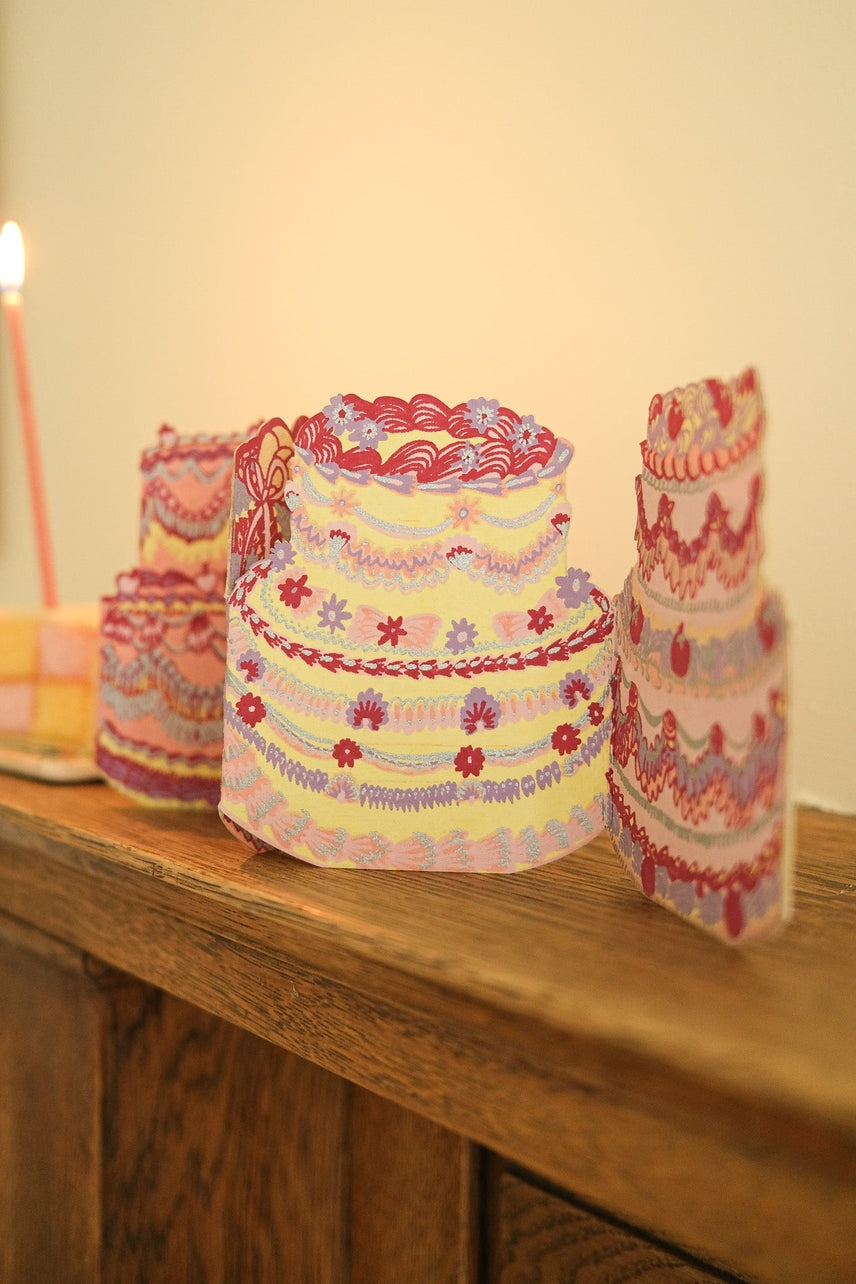 Decorative cake-shaped card on a wooden surface with a candle in the background.