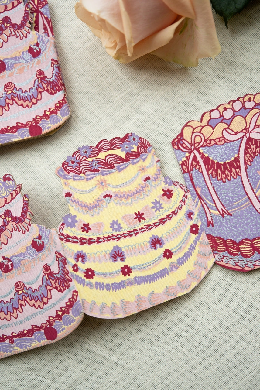 Colorful cake-shaped greeting card on a textured surface with a rose in the background.