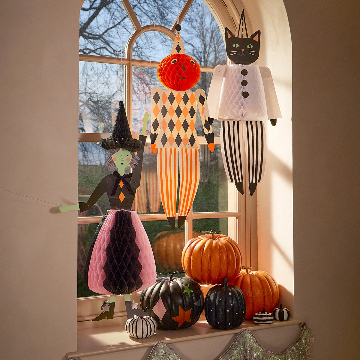 Halloween-themed decorations including a witch, cat, and harlequin figure in front of a window with pumpkins.