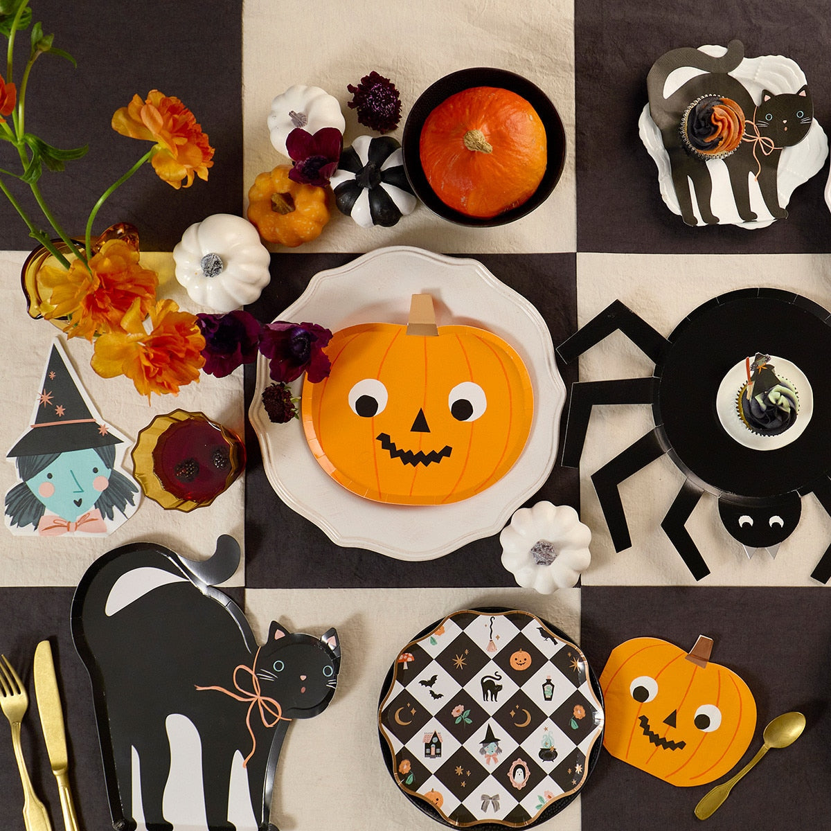 Halloween-themed table setting with decorative plates, pumpkins, and black cats on a checkered tablecloth.