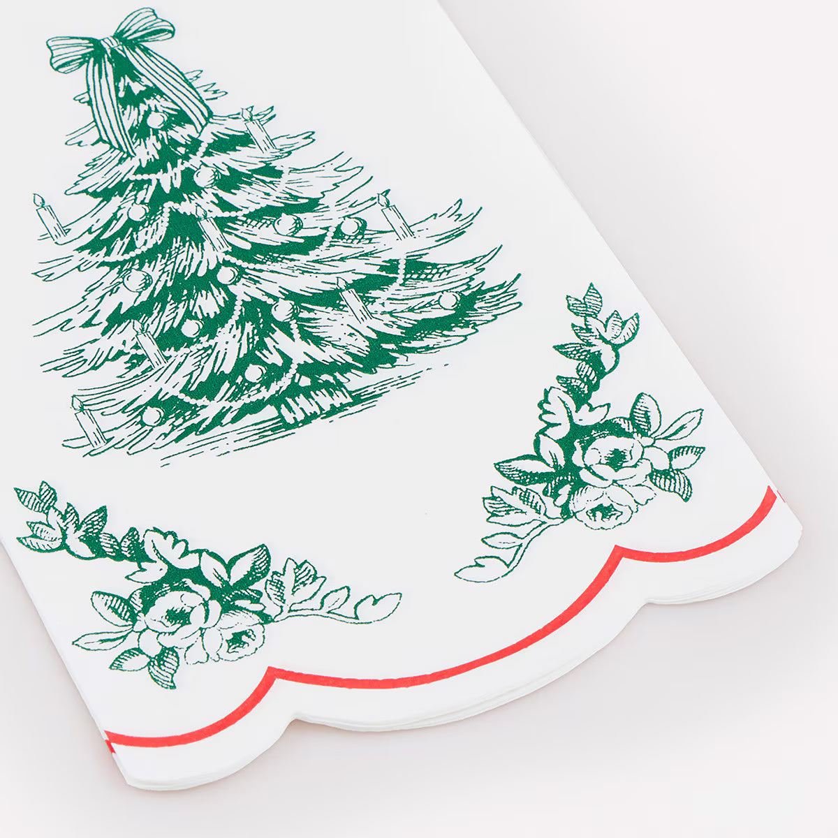 A white kitchen towel with a green Christmas tree and floral pattern, finished with a scalloped edge and a thin red line.