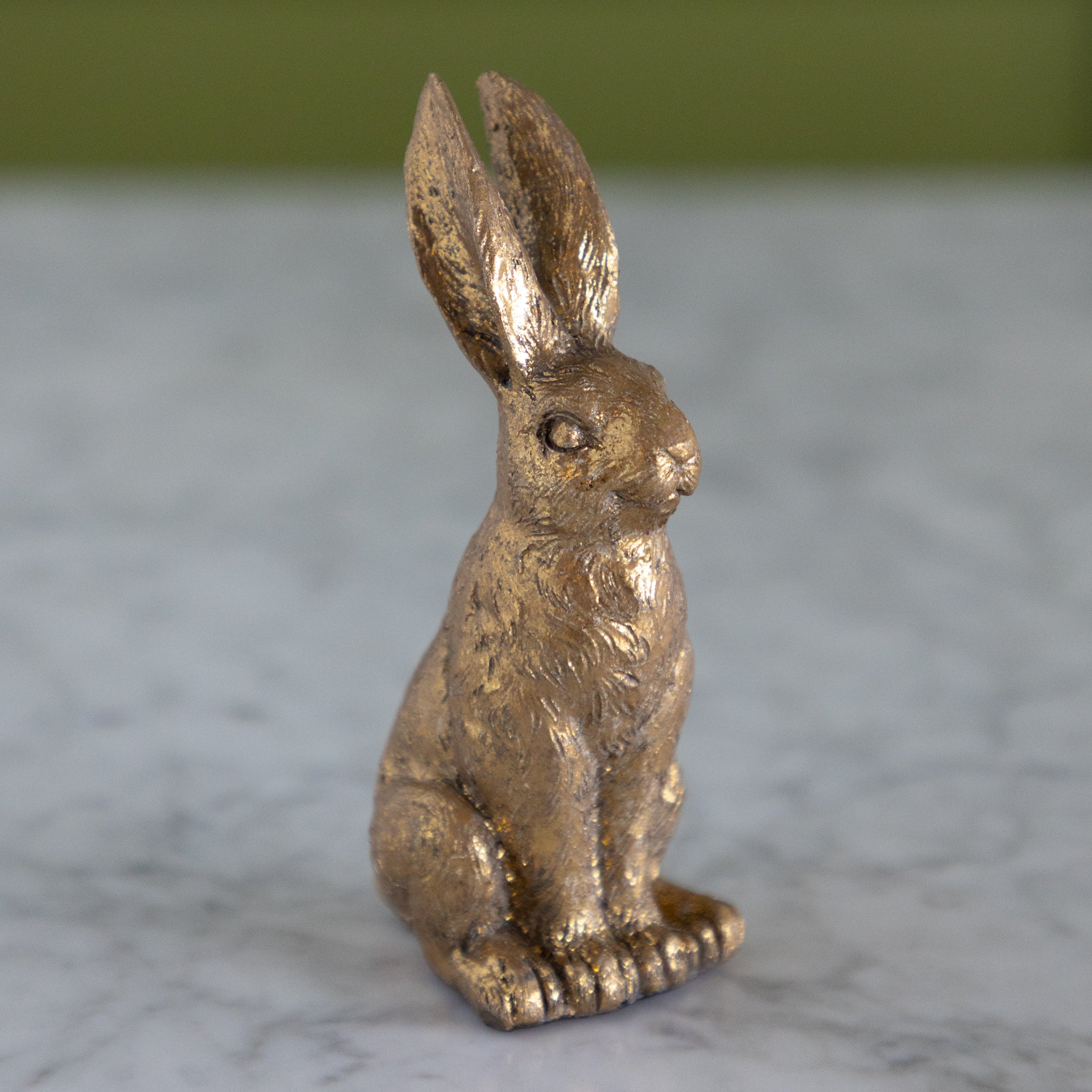Bronze rabbit figurine on a marble surface with a green background.