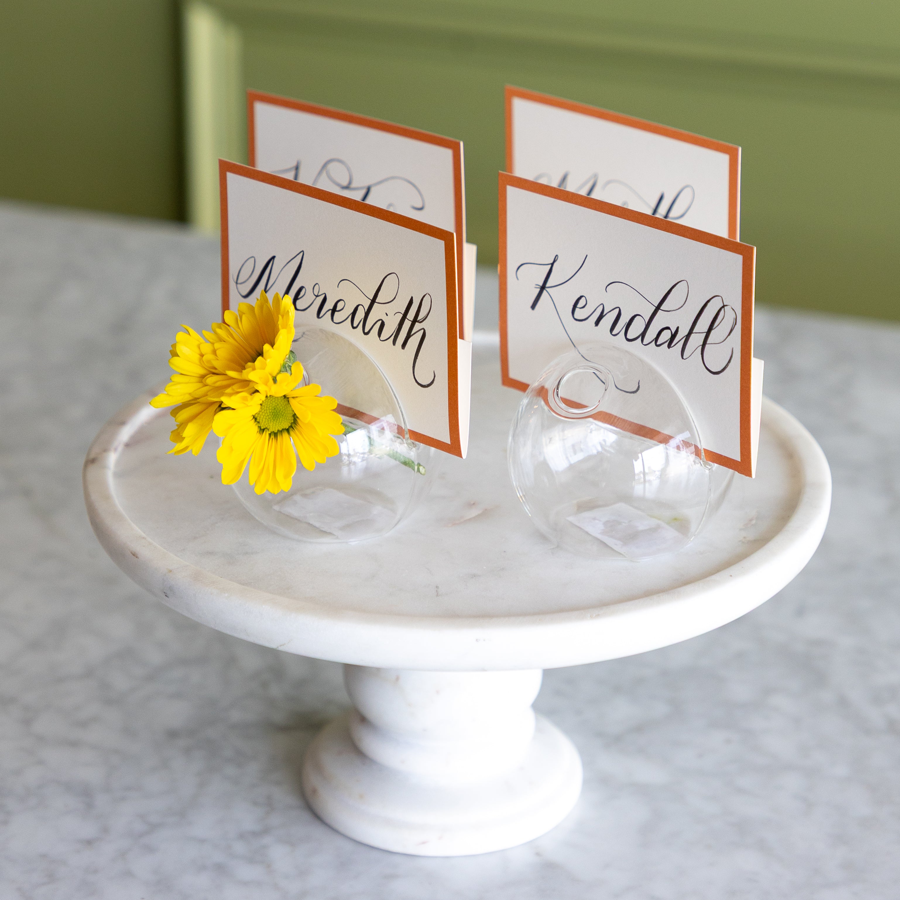 White marble cake stand with clear glass holders and name cards on a light gray surface.