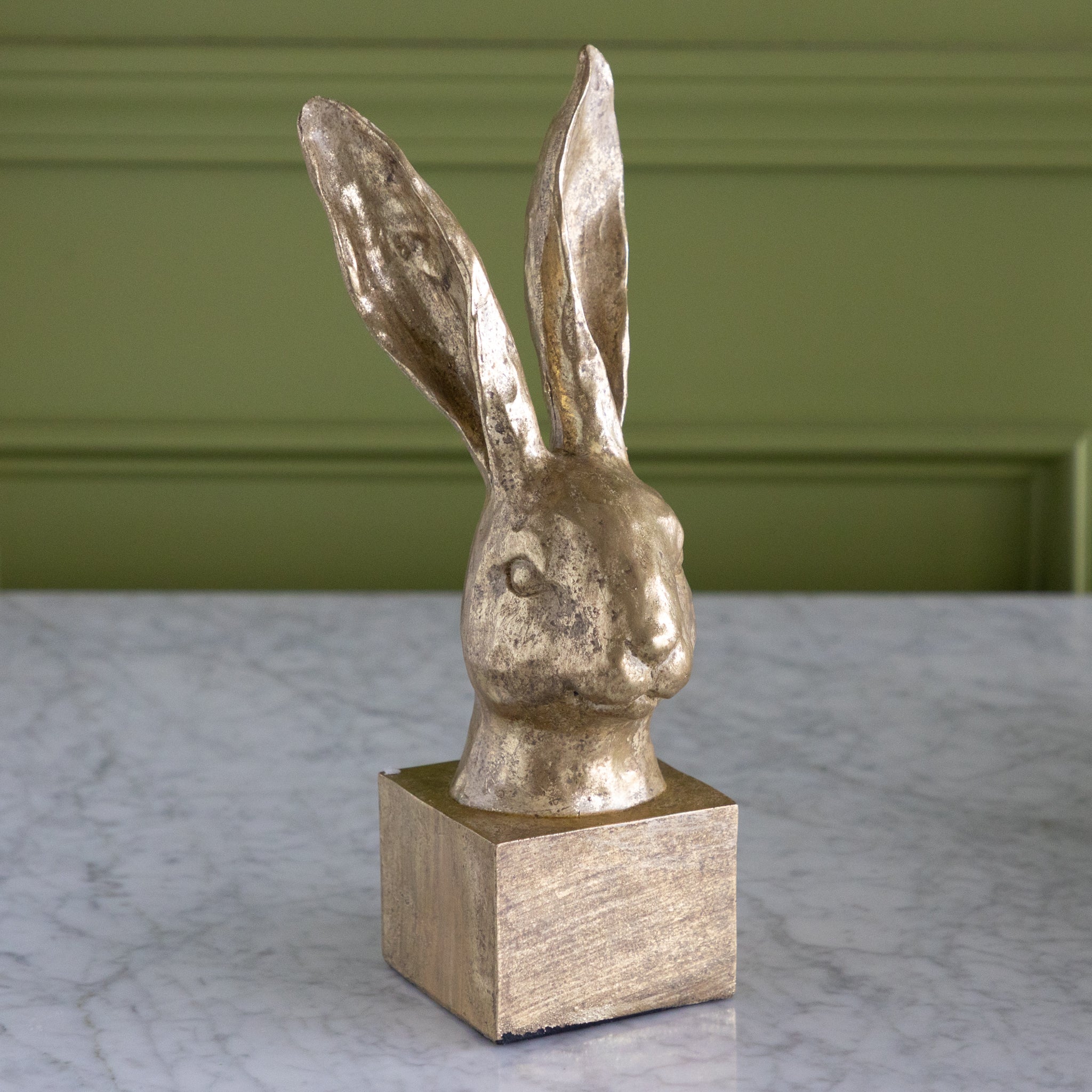 Decorative rabbit head sculpture on a square base against a green wall.
