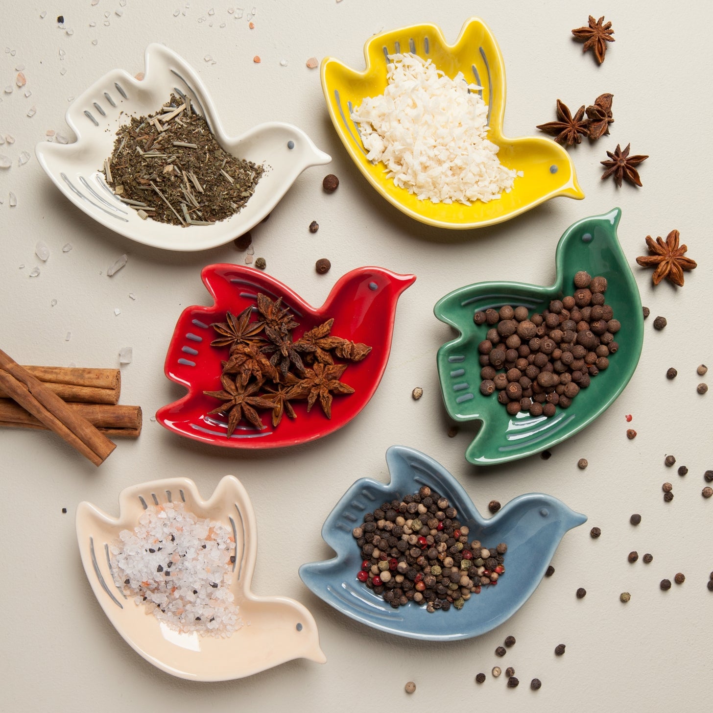 Colorful bird-shaped ceramic dishes filled with various spices and grains on a light background.