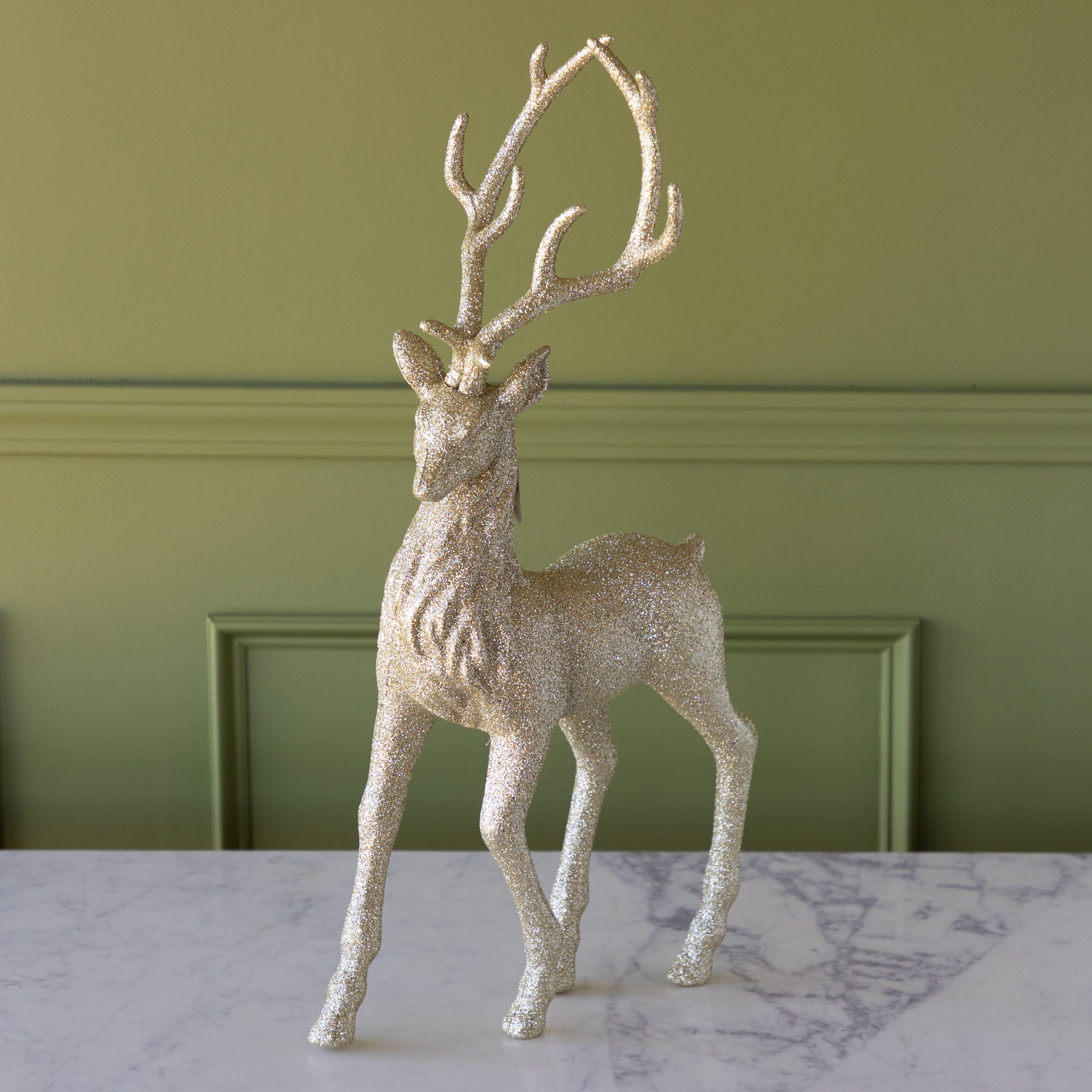 Decorative deer figurine with glittery texture on a marble surface against a green wall.
