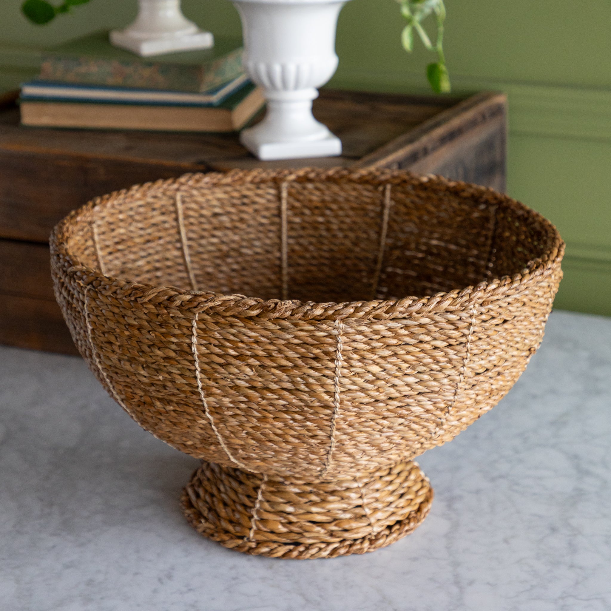 Natural Rope Weave Bowl on marble surface with a wooden box, books and a plant in the background.