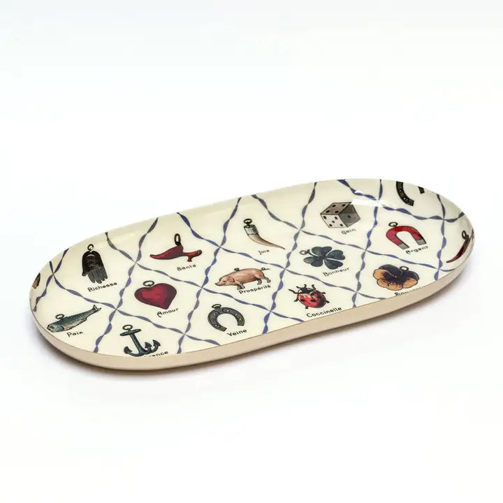 An oval shaped enamel plate containing a pattern of illustrated charms including a horseshoe, a lady bug, a four-leafed clover, and other symbols of luck.