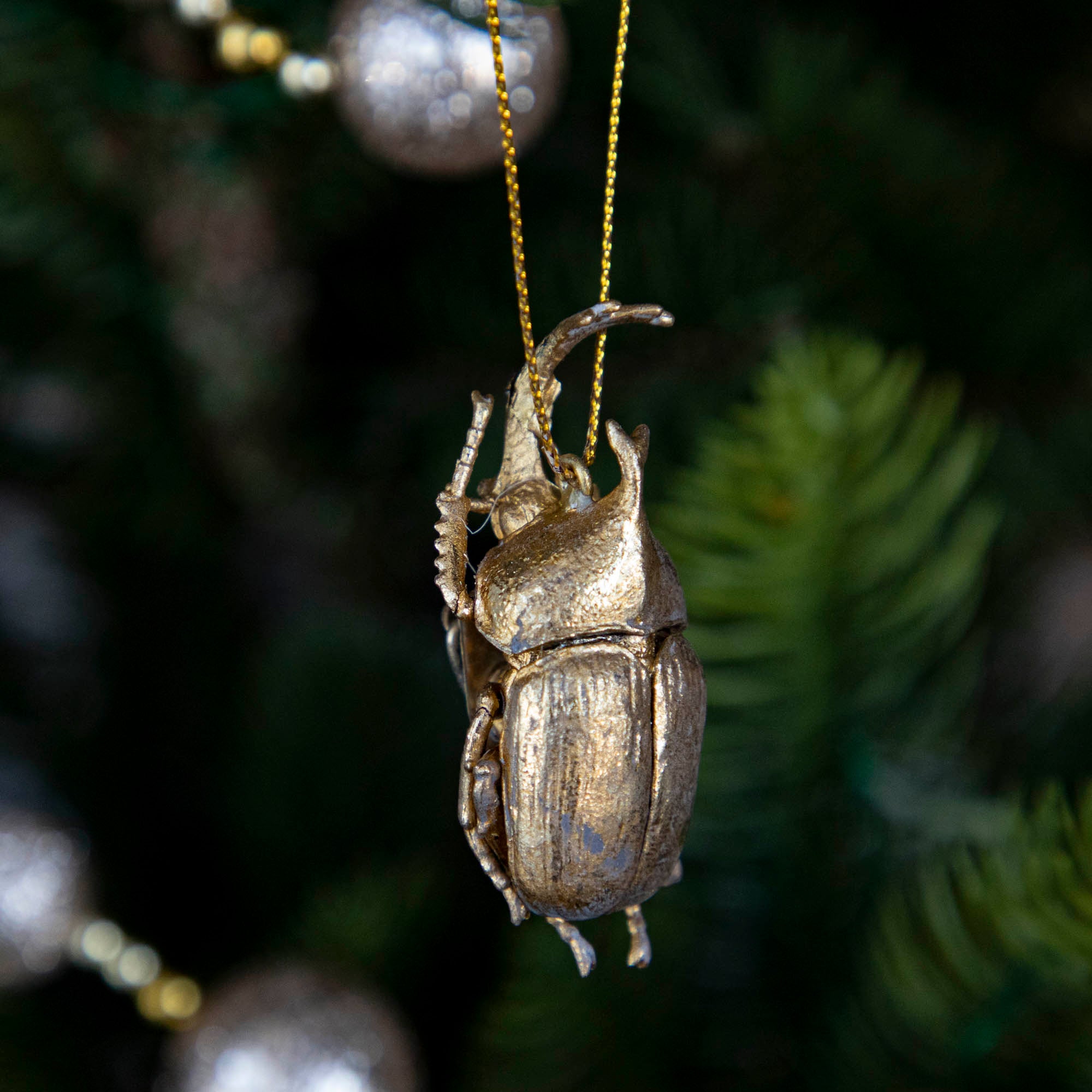 Gold-colored metal beetle-shaped ornament hanging on a Christmas tree.