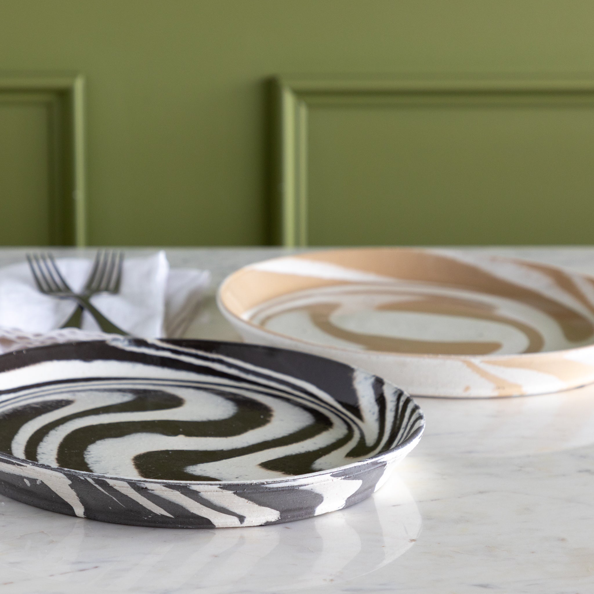 Two marbled patterned plates on a marble surface with a green wall background.