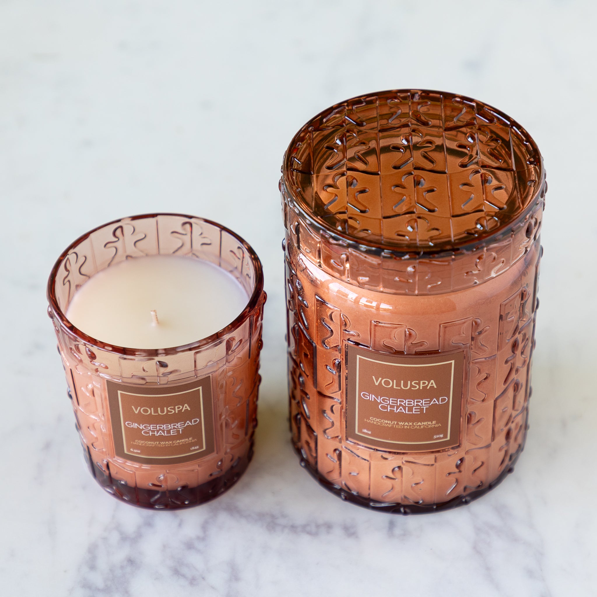 Two Voluspa candles with decorative glass containers on a marble surface.