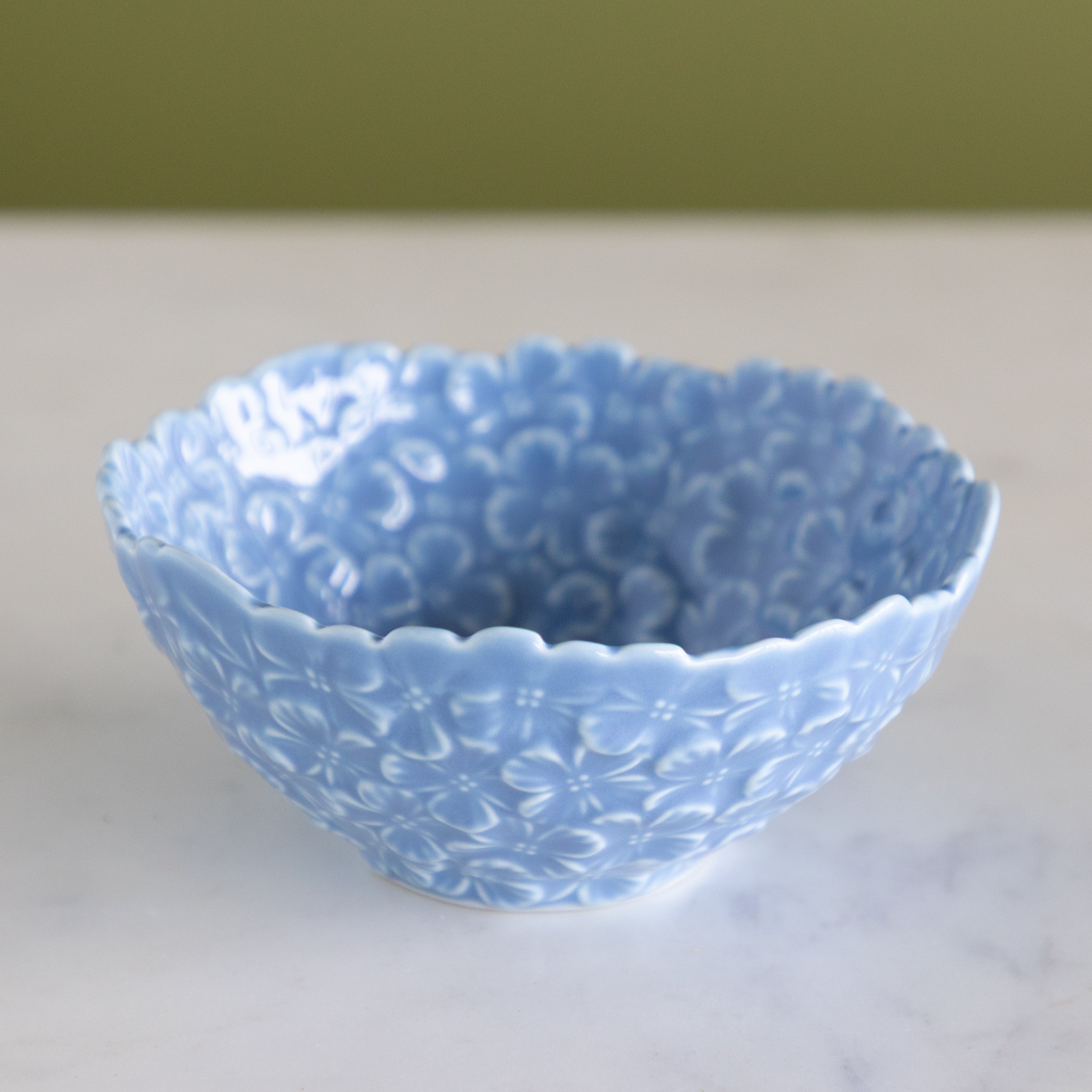 Blue ceramic bowl with hydrangea pattern on a white surface with a green background.
