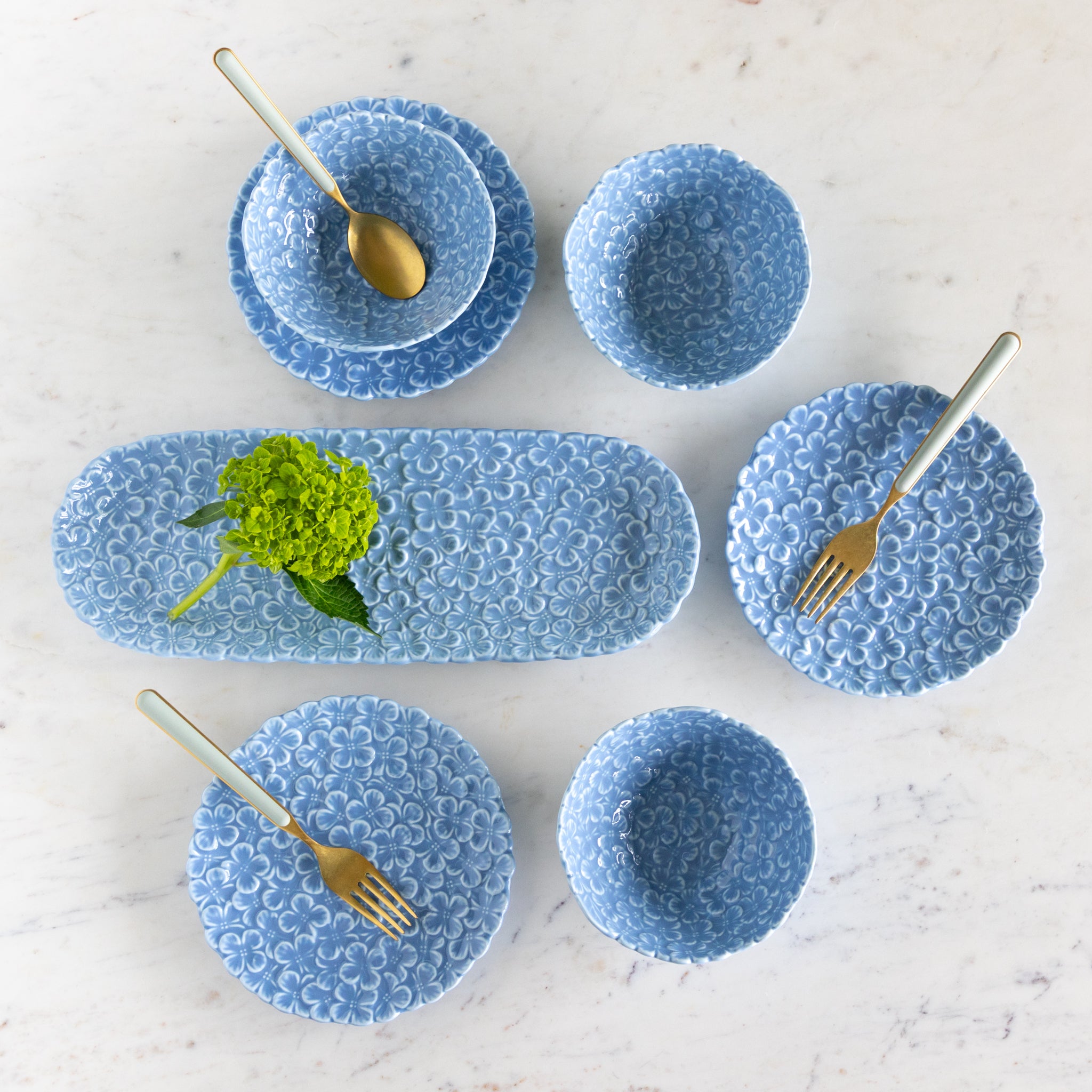 Set of blue textured ceramic dishes with gold cutlery on a light background.
