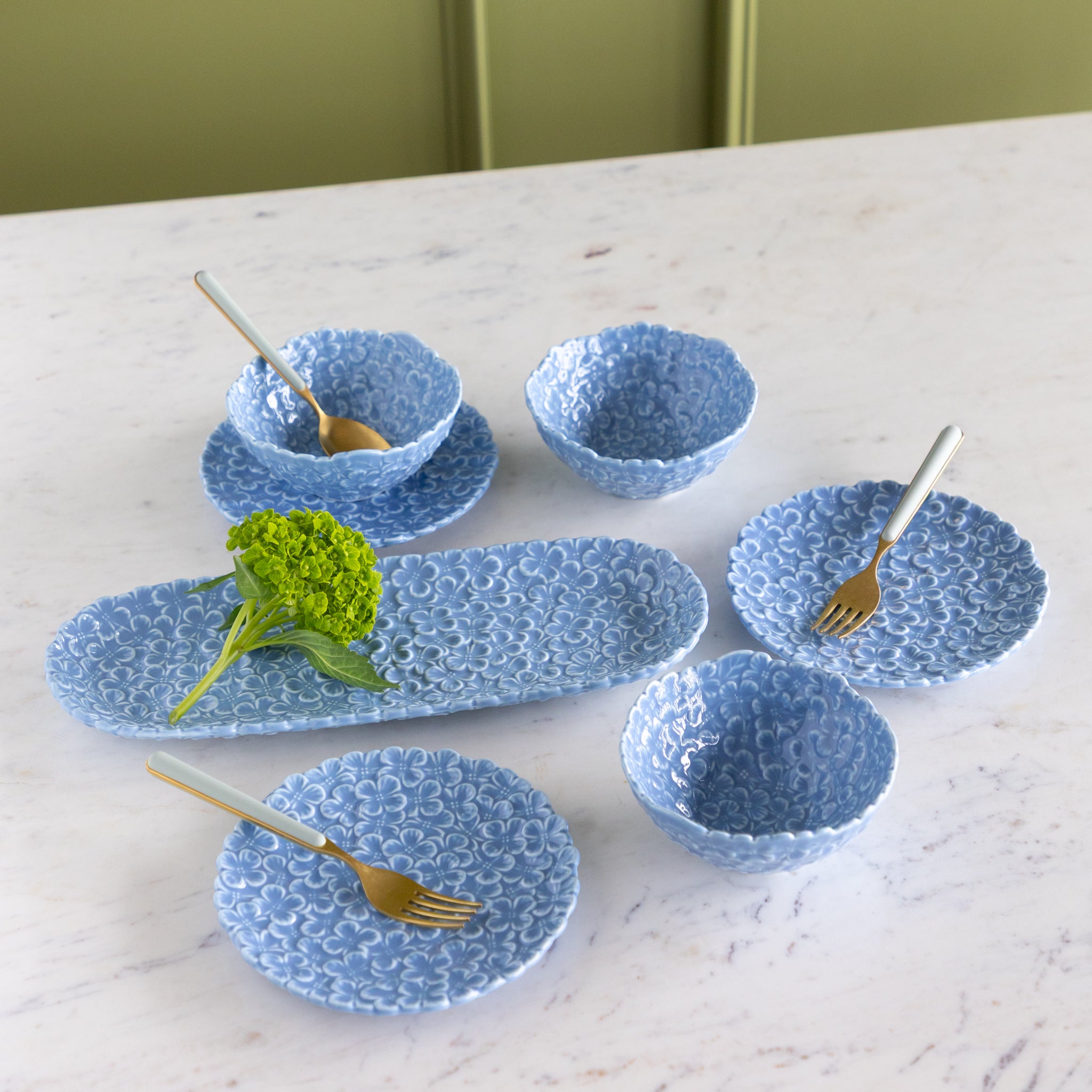 Set of blue textured ceramic dishes on a marble surface with gold forks.